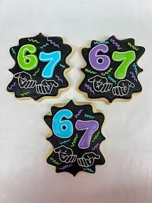 Three black cookies decorated with colorful numbers and accessories for a birthday celebration, displaying the numbers 6 and 7.