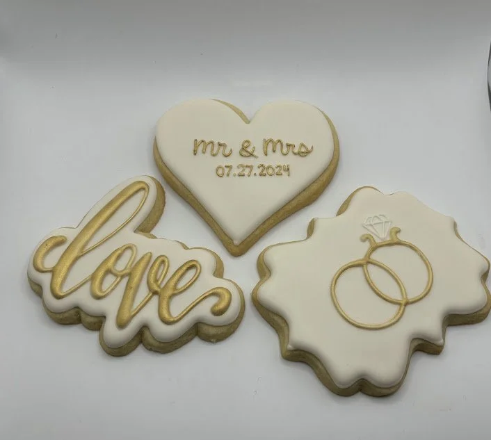 Decorative cookies with wedding themes, including a heart-shaped cookie with "mr & mrs" and a date, a cookie with the word "love" in script, and a cookie with two wedding rings depicted.