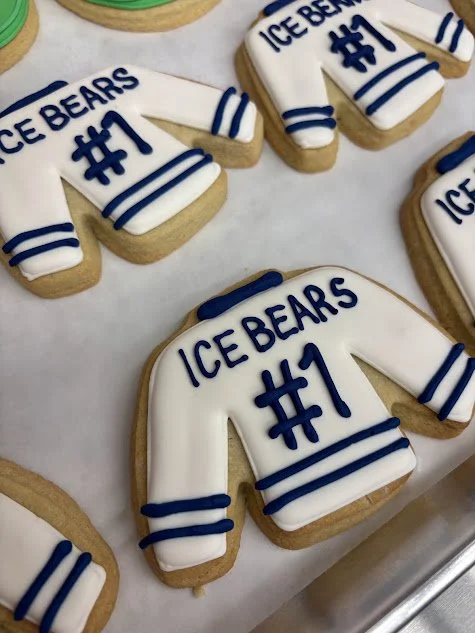 Decorated football-shaped sugar cookies with white icing and blue writing that say 'Ice Bears #1' and have striped details.