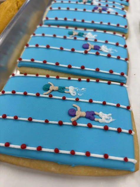 A row of decorated cookies with blue icing, small red and white sugar beads, and tiny figurines of astronauts in space suits.