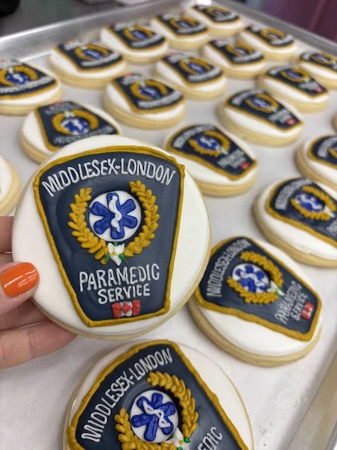 Decorated cookies in the shape of Middlesex-London Paramedic Service badges on a tray.