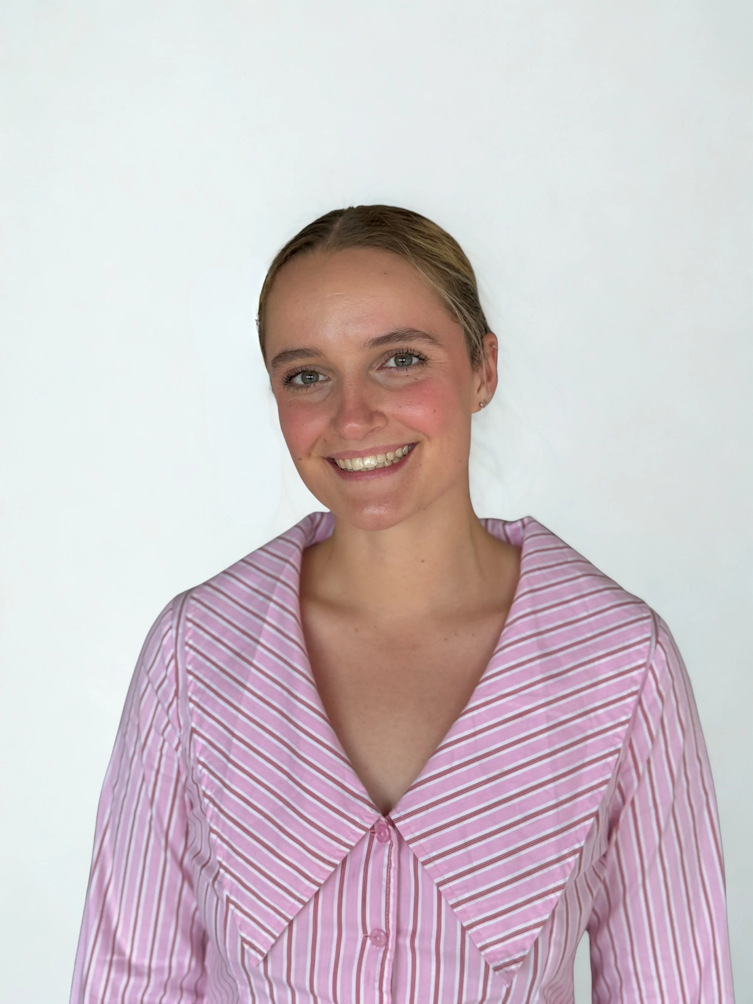 A woman smiling and wearing a pink and white striped shirt, with her hair pulled back against a plain white background.