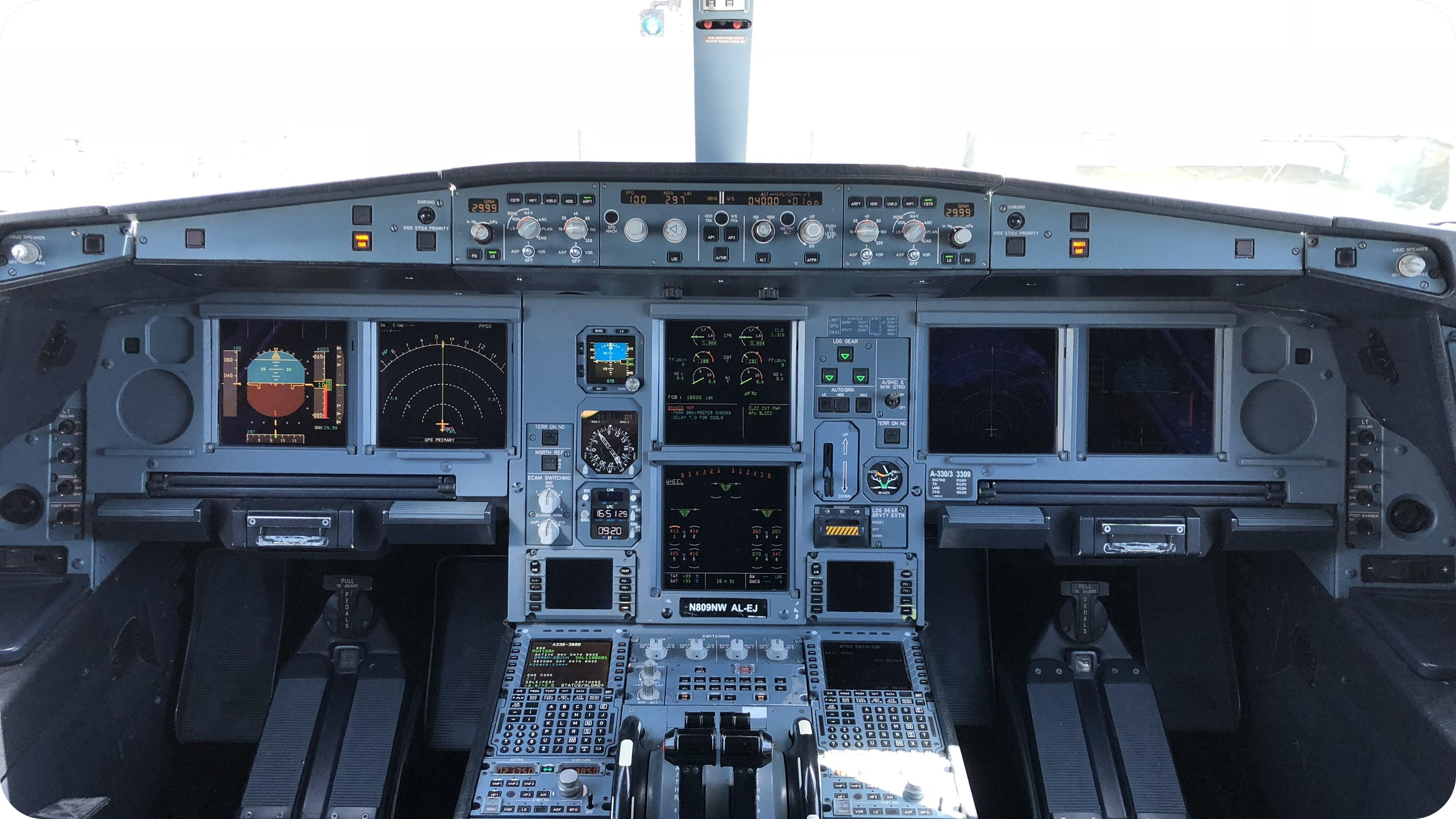 The cockpit of an airplane with various digital and analog displays, controls, and gauges, including a central display with flight information and two large screens on each side.
