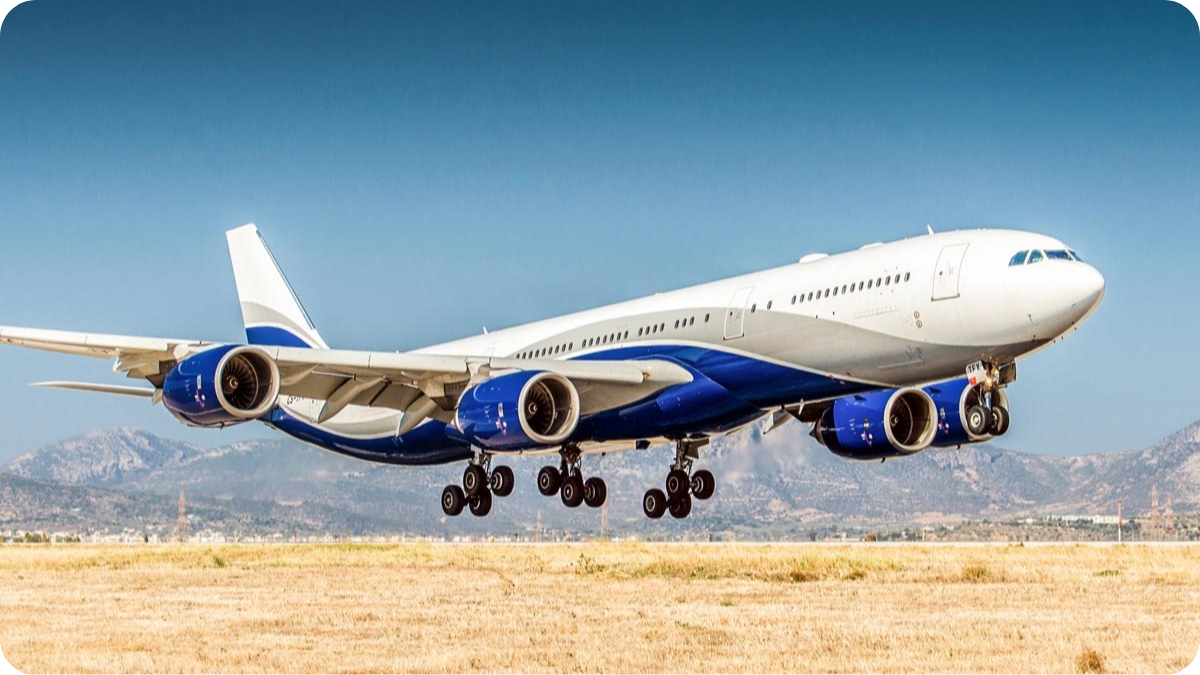 A large commercial airplane with a white fuselage and blue accents on the engines and underside of the wings, landing on an airport runway with a mountain range in the background.