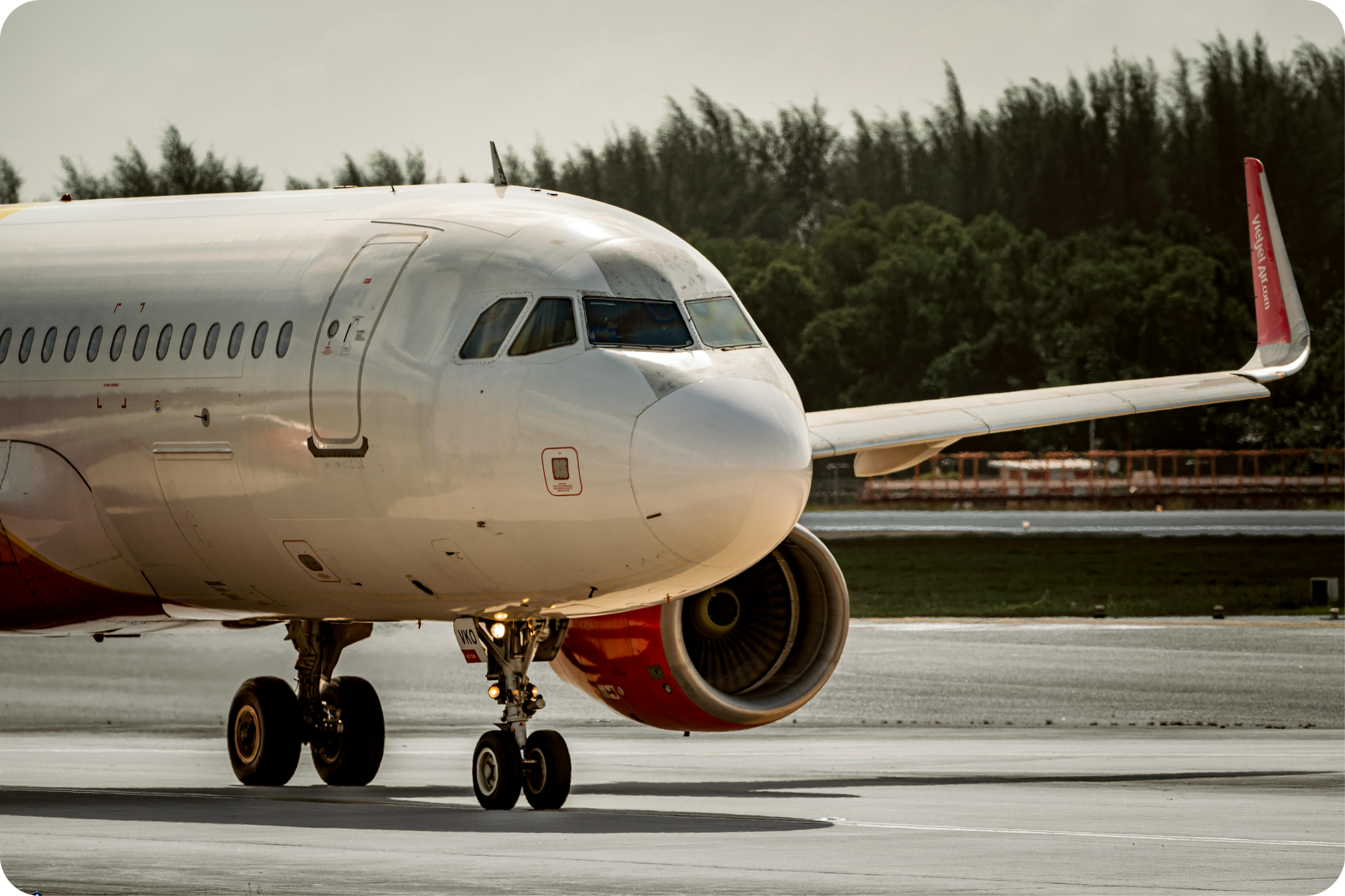Close-up of a white commercial airplane taxiing on the runway with a green, tree-lined background.