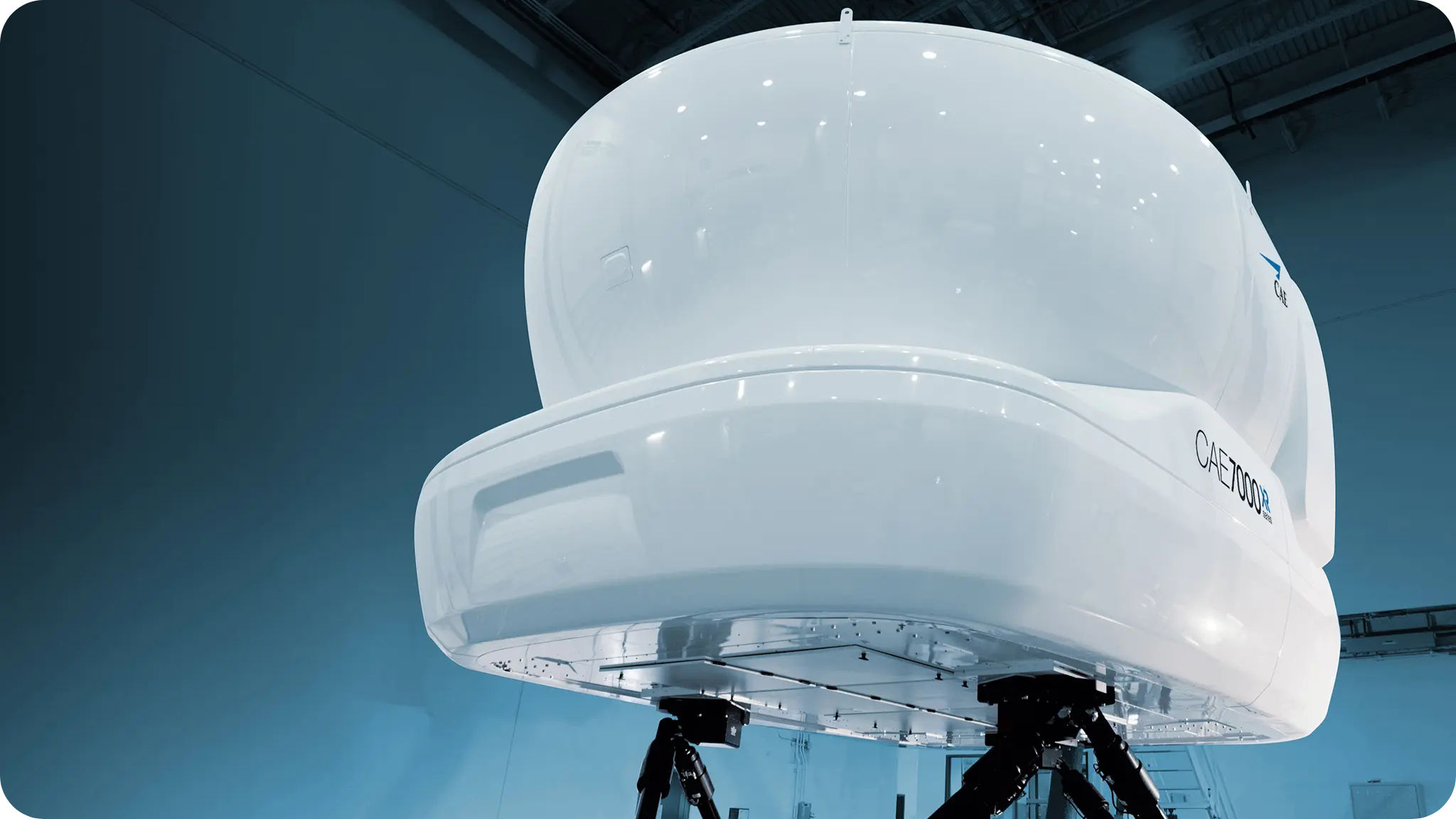 A large white spacecraft or satellite with a dome-like structure on top, mounted on a black tripod stand inside a high-ceilinged lab or hangar.
