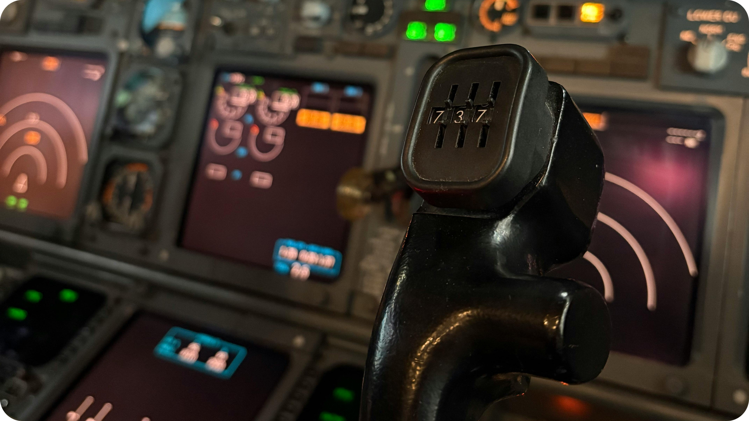 Close-up view of an airplane throttle lever with the speed brake toggle on top, with various flight instruments and cockpit displays visible in the background.