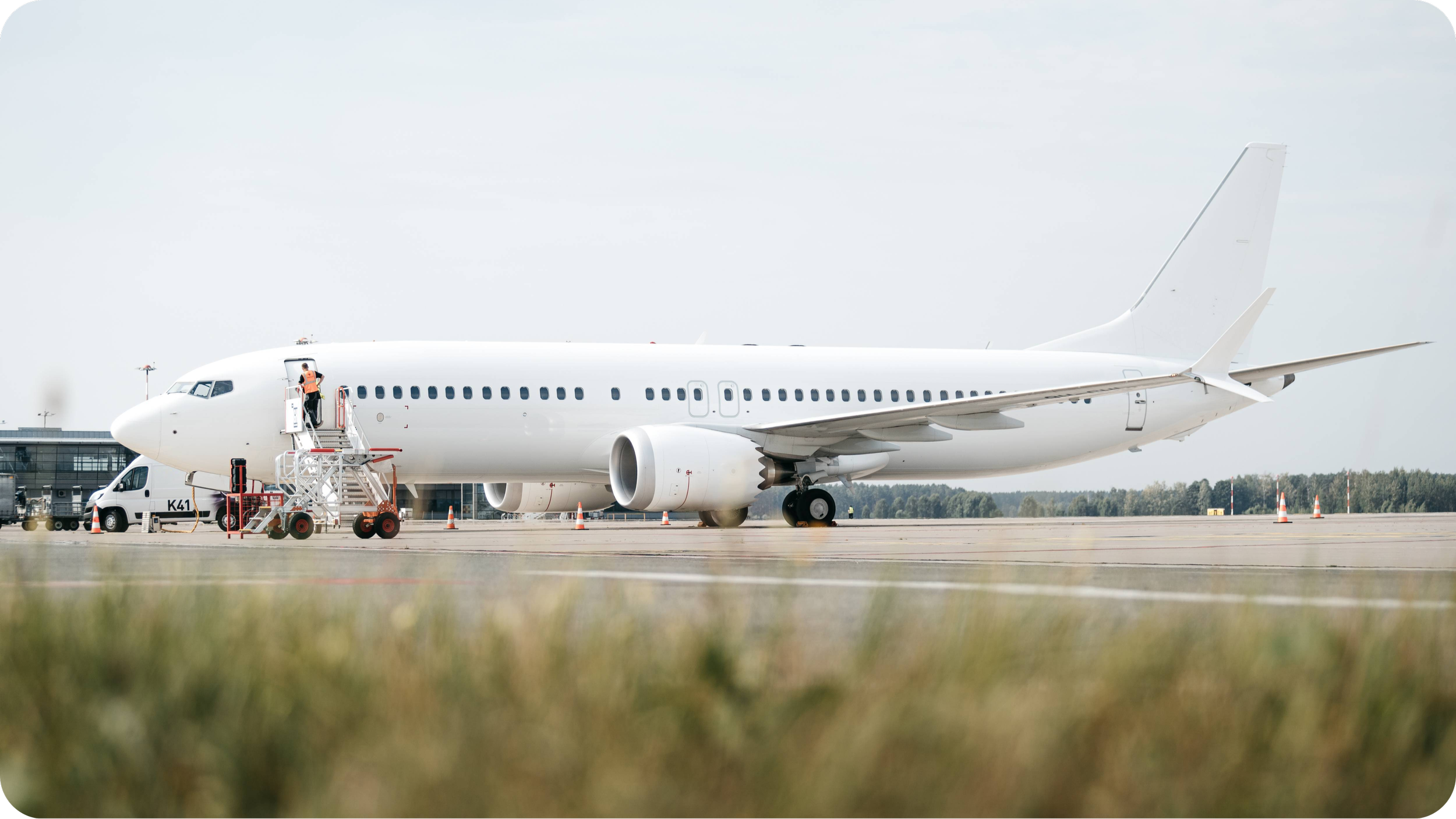 A white commercial airplane parked on the tarmac at an airport with ground crew preparing the aircraft.