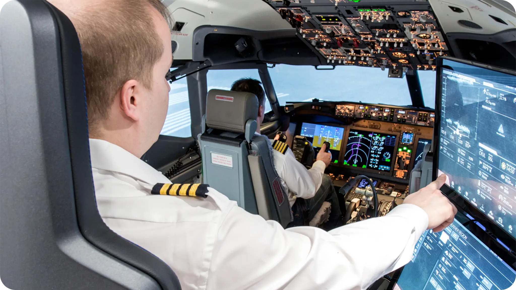 Two airline pilots in a cockpit, with one pilot pointing at a touchscreen display on the right, and various instruments and controls on the dashboards.