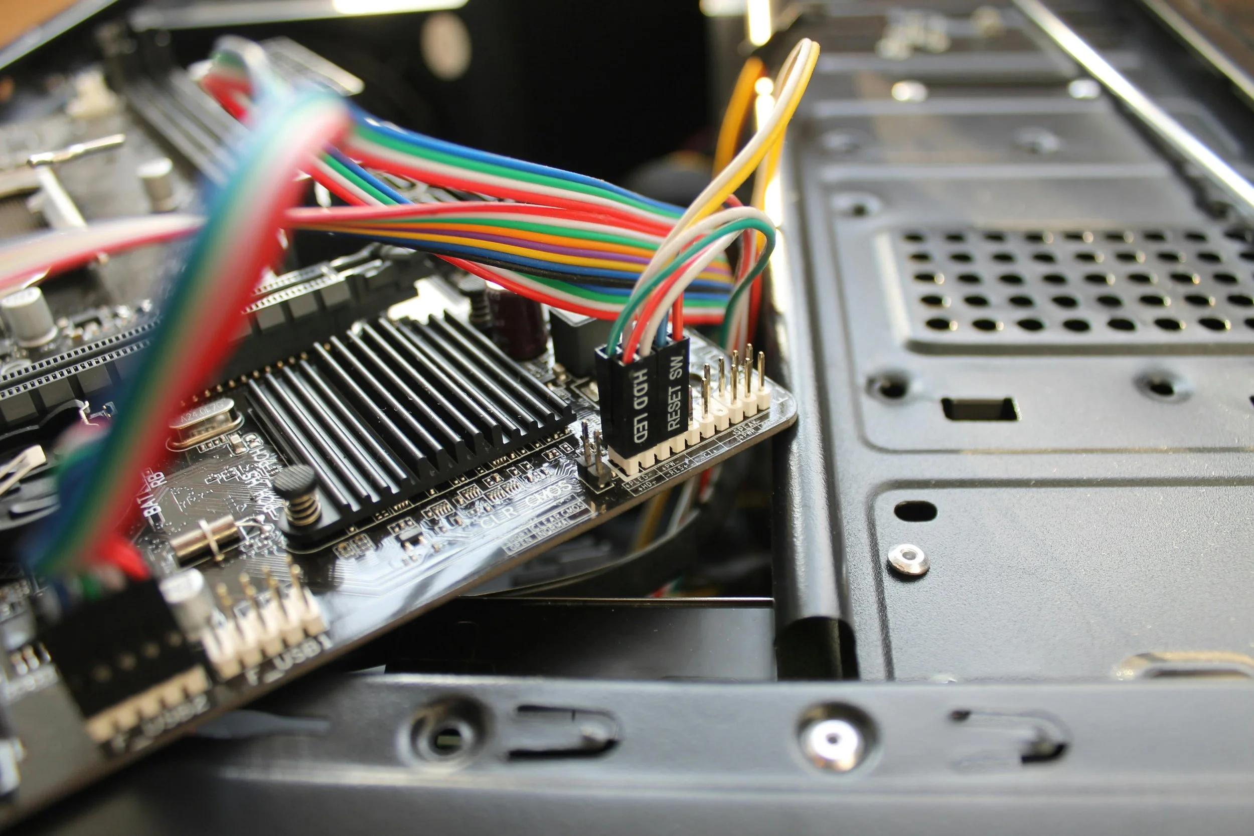 Inside a computer case, a motherboard with connected multicolored wires and a heatsink.
