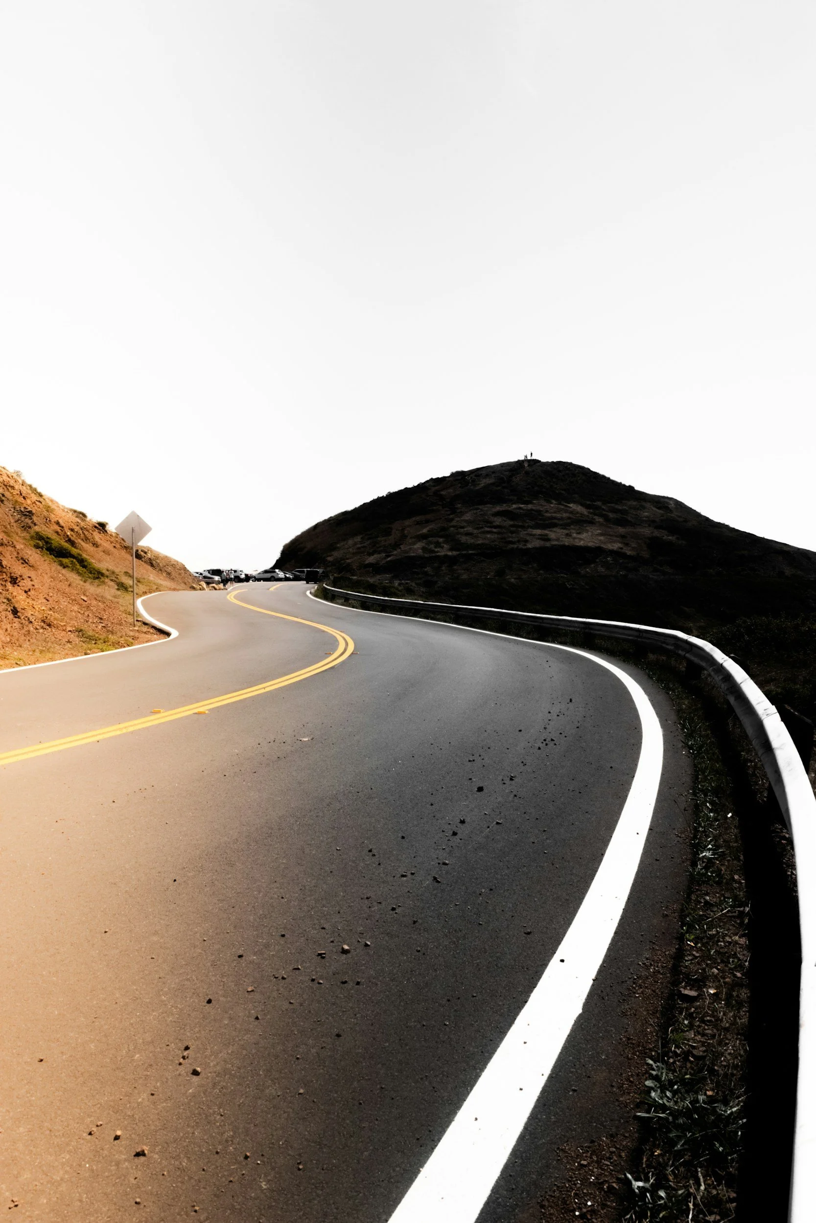 Winding mountain road with guardrail and a hill in the distance.