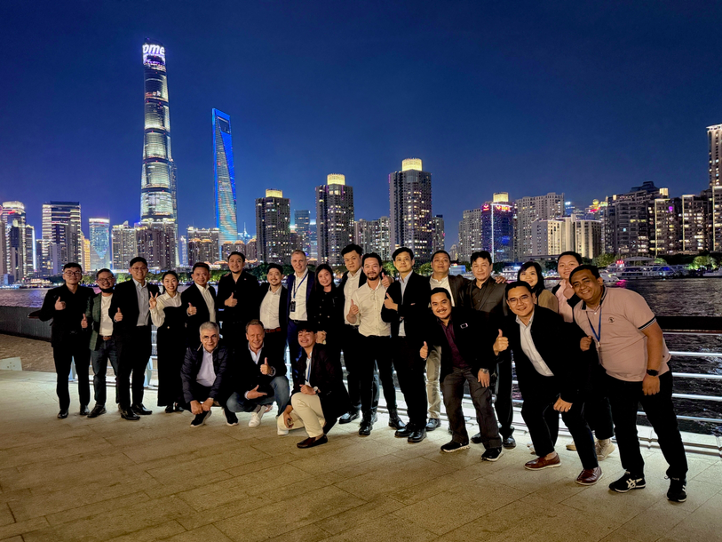 Group of people posing on a waterfront promenade at night with a city skyline and illuminated skyscrapers in the background.