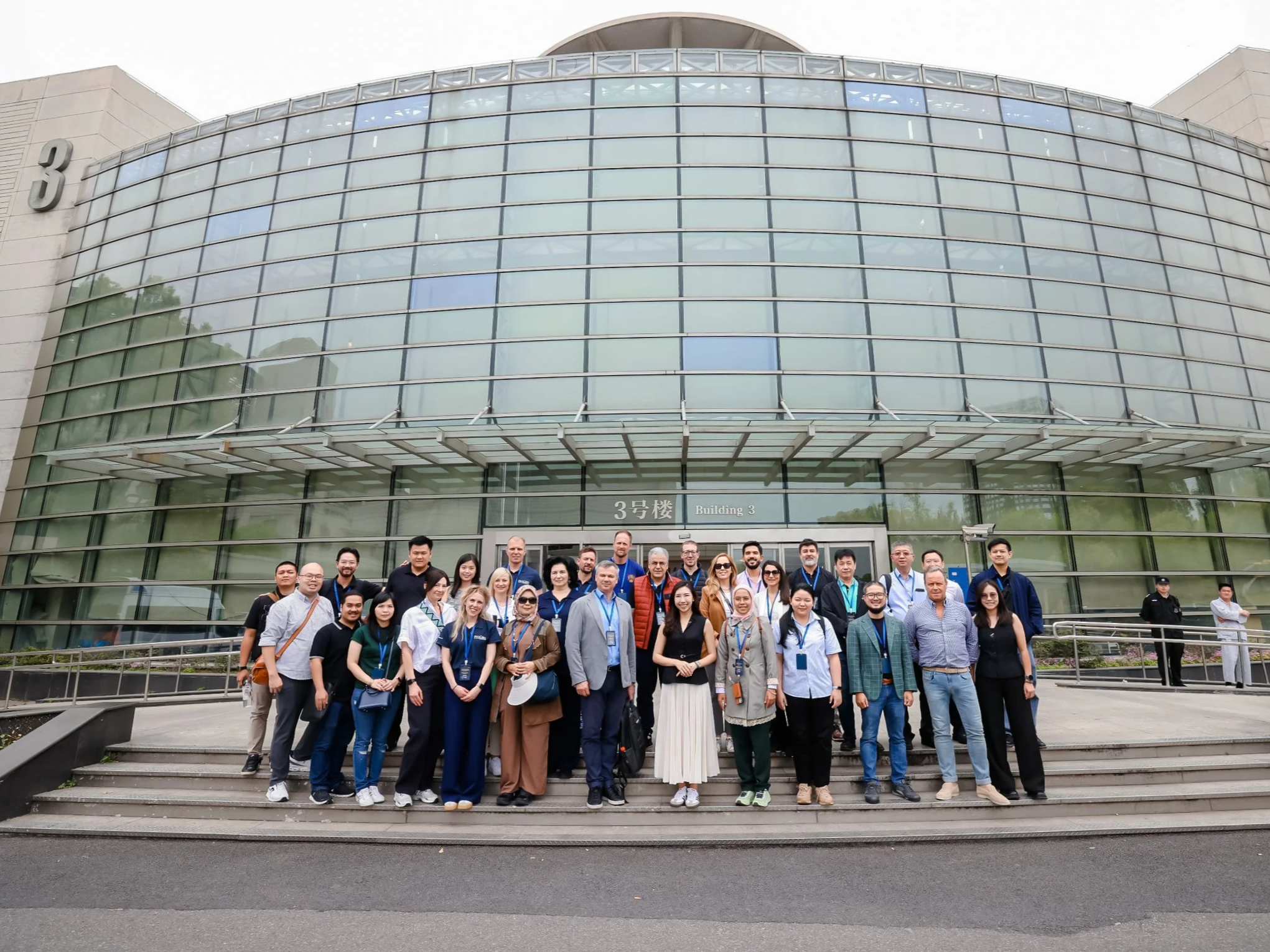 A group of diverse people standing on stairs in front of a modern glass building labeled 'Building 3'