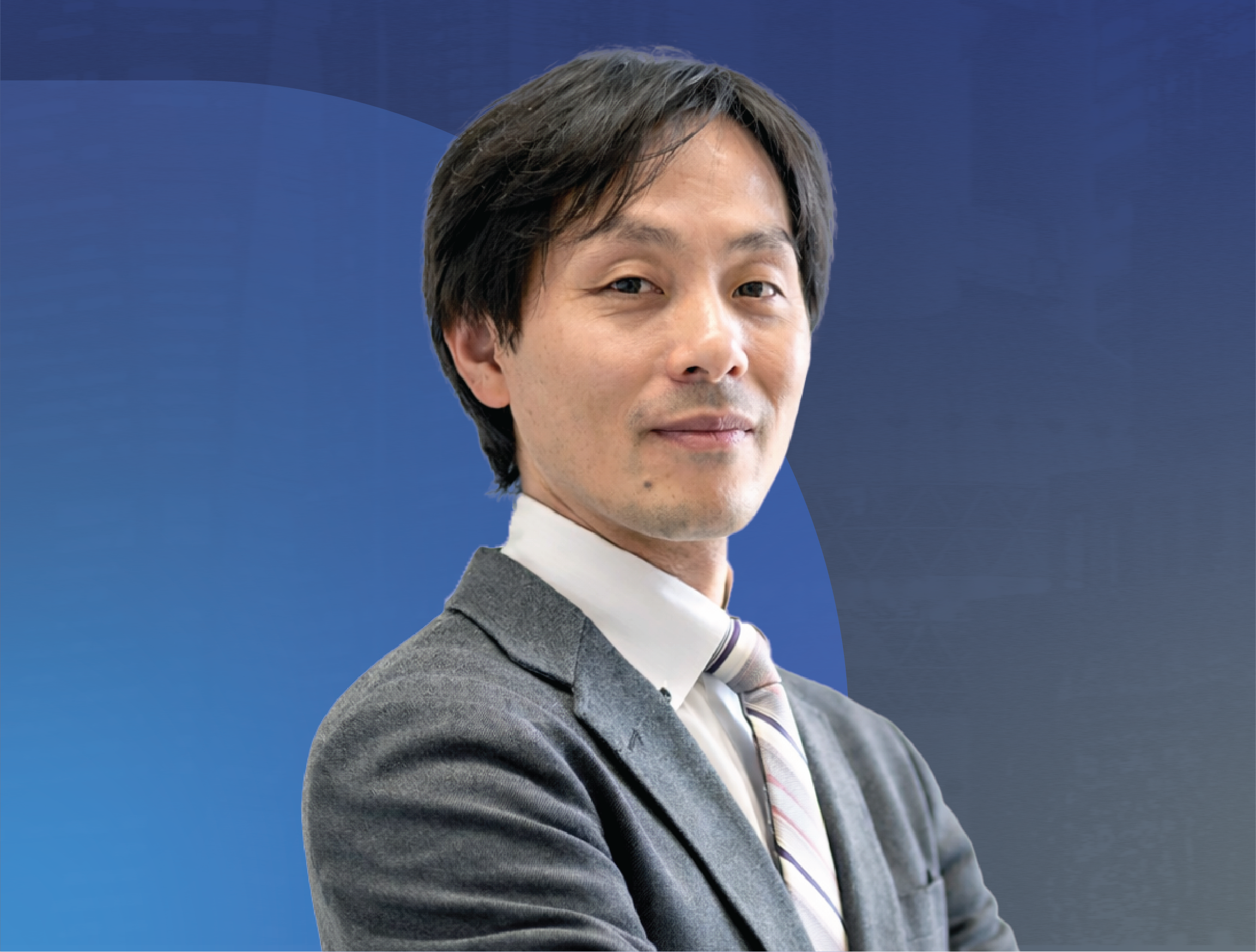 Portrait of Professor Shingo Shimoda from Nagoya University with dark hair wearing a gray suit and striped tie, smiling calmly against a blue background.