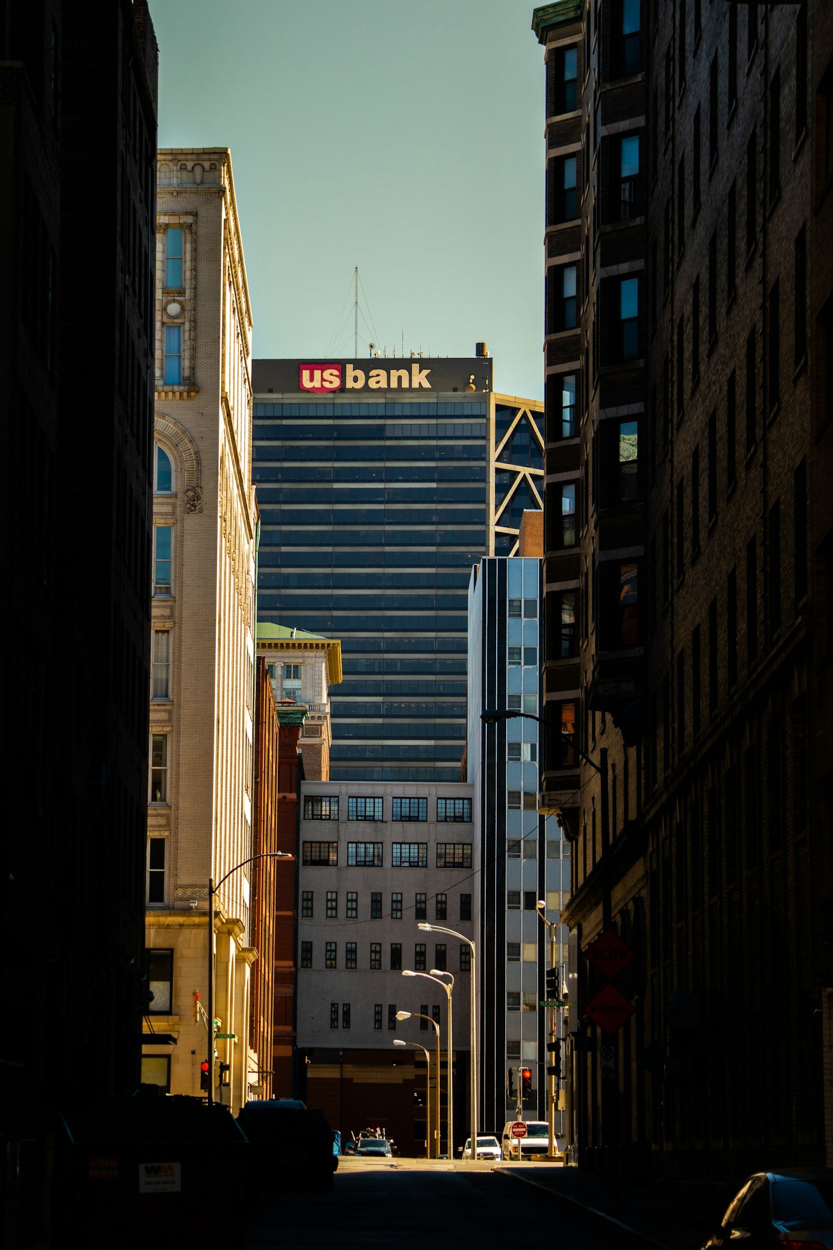 City street with tall buildings, US Bank sign on a skyscraper, view down a dark alley with cars and streetlights, clear sky.