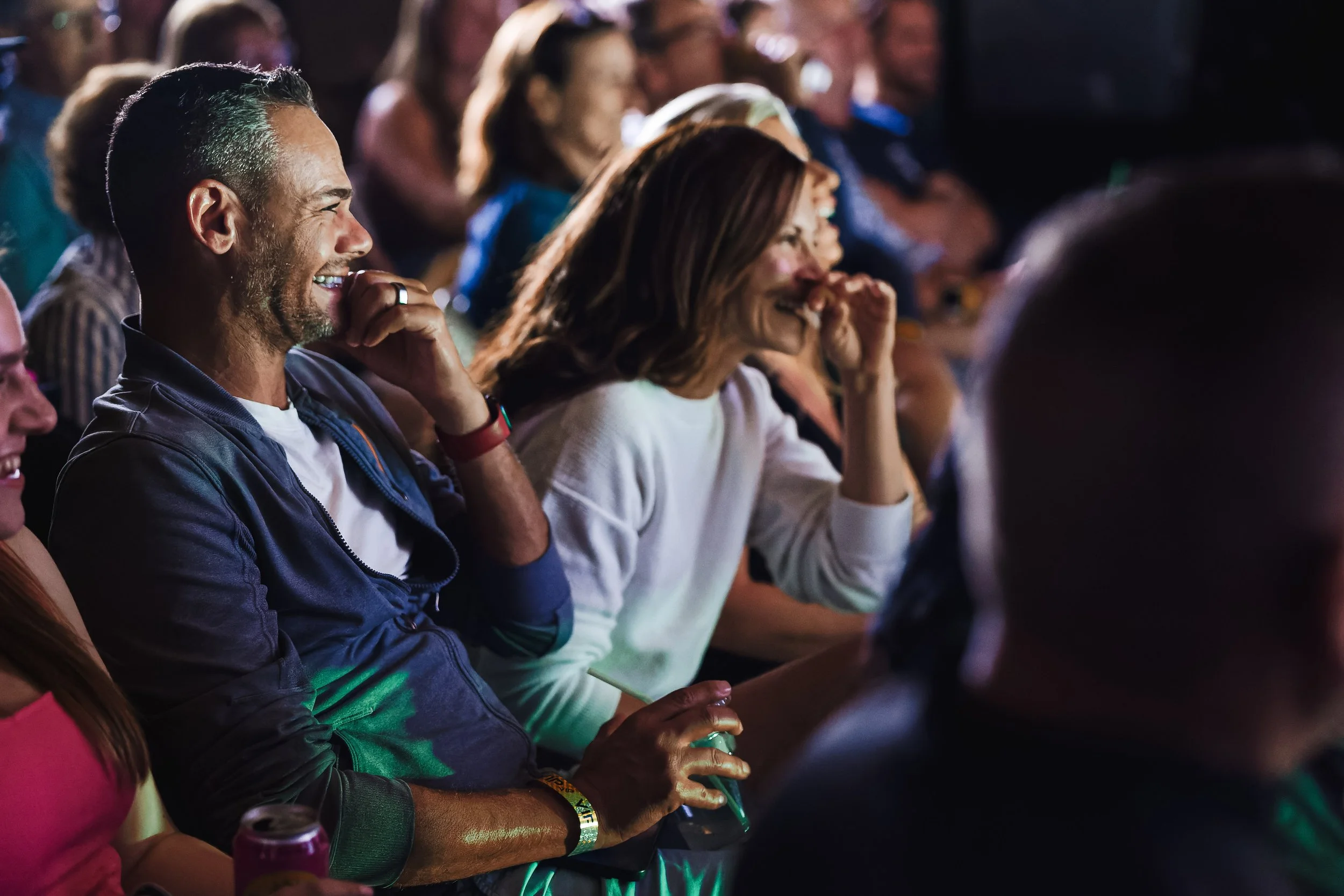 Group of people sitting in an audience, laughing and enjoying a performance or speech at an event, with expressions of happiness and amusement.