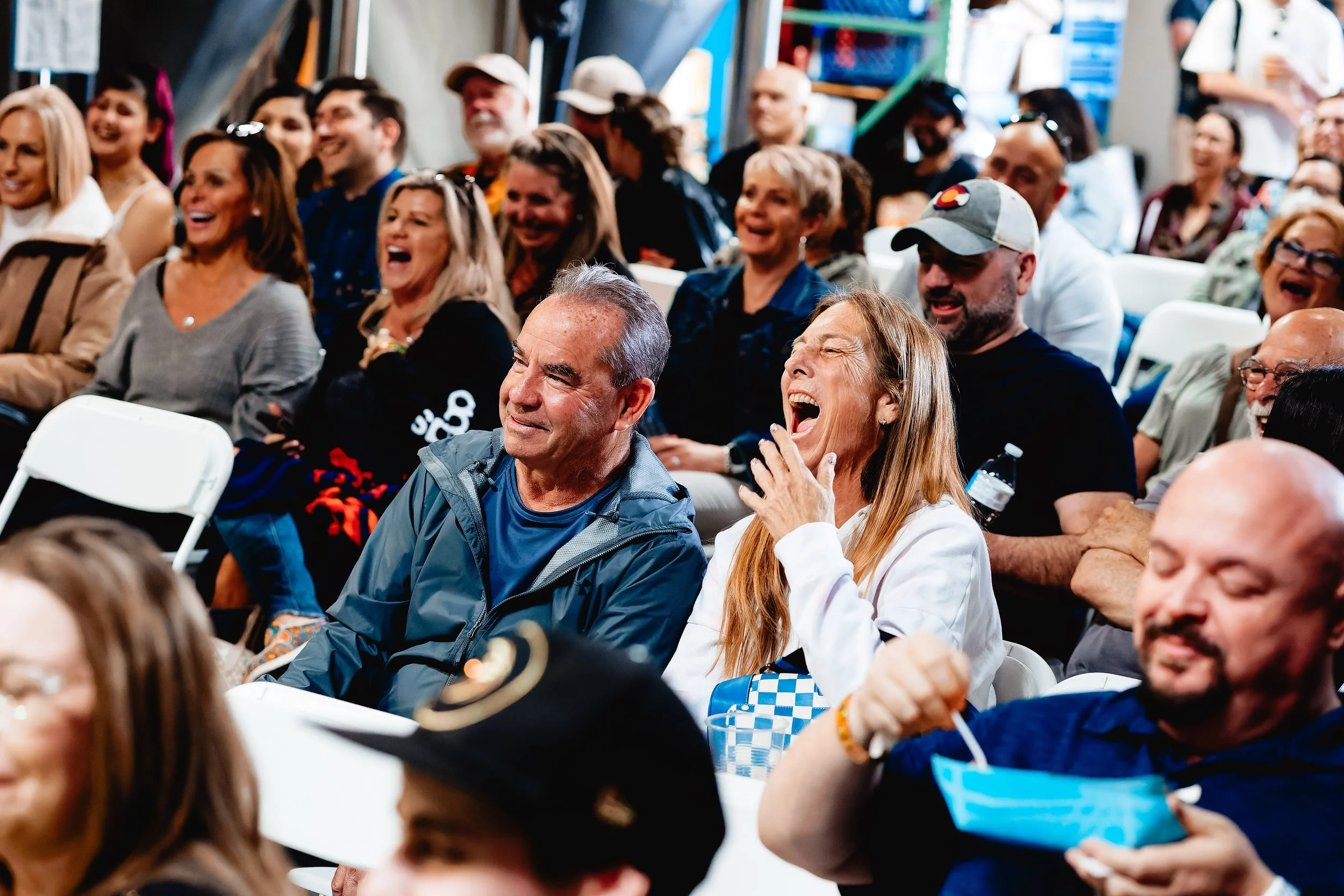 A diverse group of people sitting in an audience, laughing and enjoying a presentation or performance.