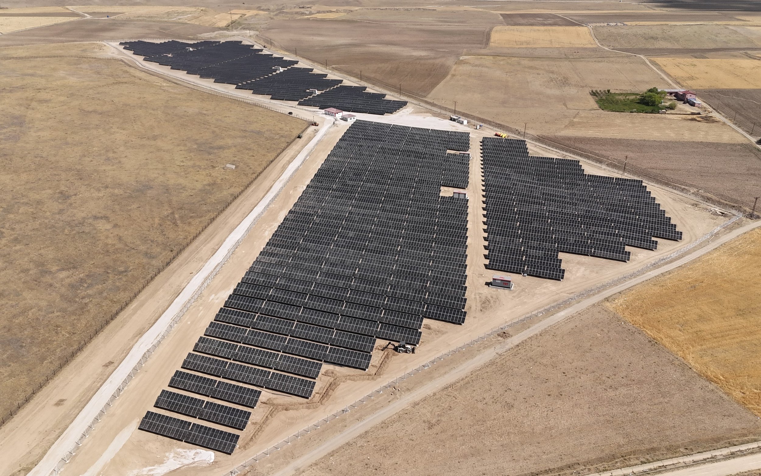 An aerial view of a large solar farm with numerous rows of solar panels installed on a flat, dry landscape.