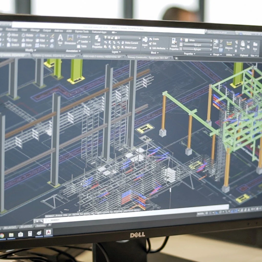 Computer monitor displaying a detailed 3D CAD drawing of an industrial construction site with structural frameworks and cranes.