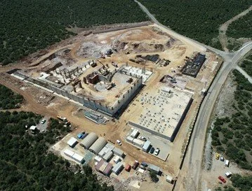 A large construction site with buildings in progress, surrounded by trees and roads.