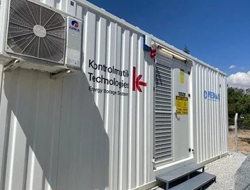 Portable energy storage system enclosed in a white container with ventilation and control panels, labeled with German text 'Kontrollierte Technologie' and an arrow pointing to a door.