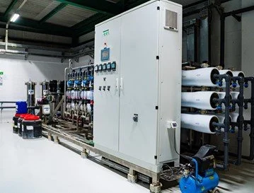 Industrial water treatment equipment with large white control panel and multiple water filter rolls in a factory.