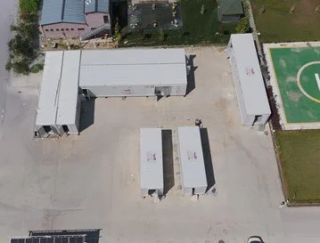 Top-down view of several metal storage containers or trailers in a paved lot with surrounding buildings and a sports field.