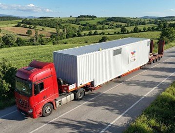 Semi-truck with a red cab and a white shipping container driving on a rural road through green fields and hills.