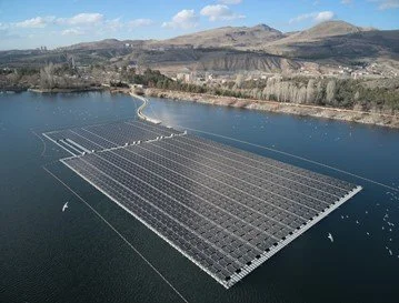 A floating solar panel farm on a lake with mountains and a partly cloudy sky in the background.
