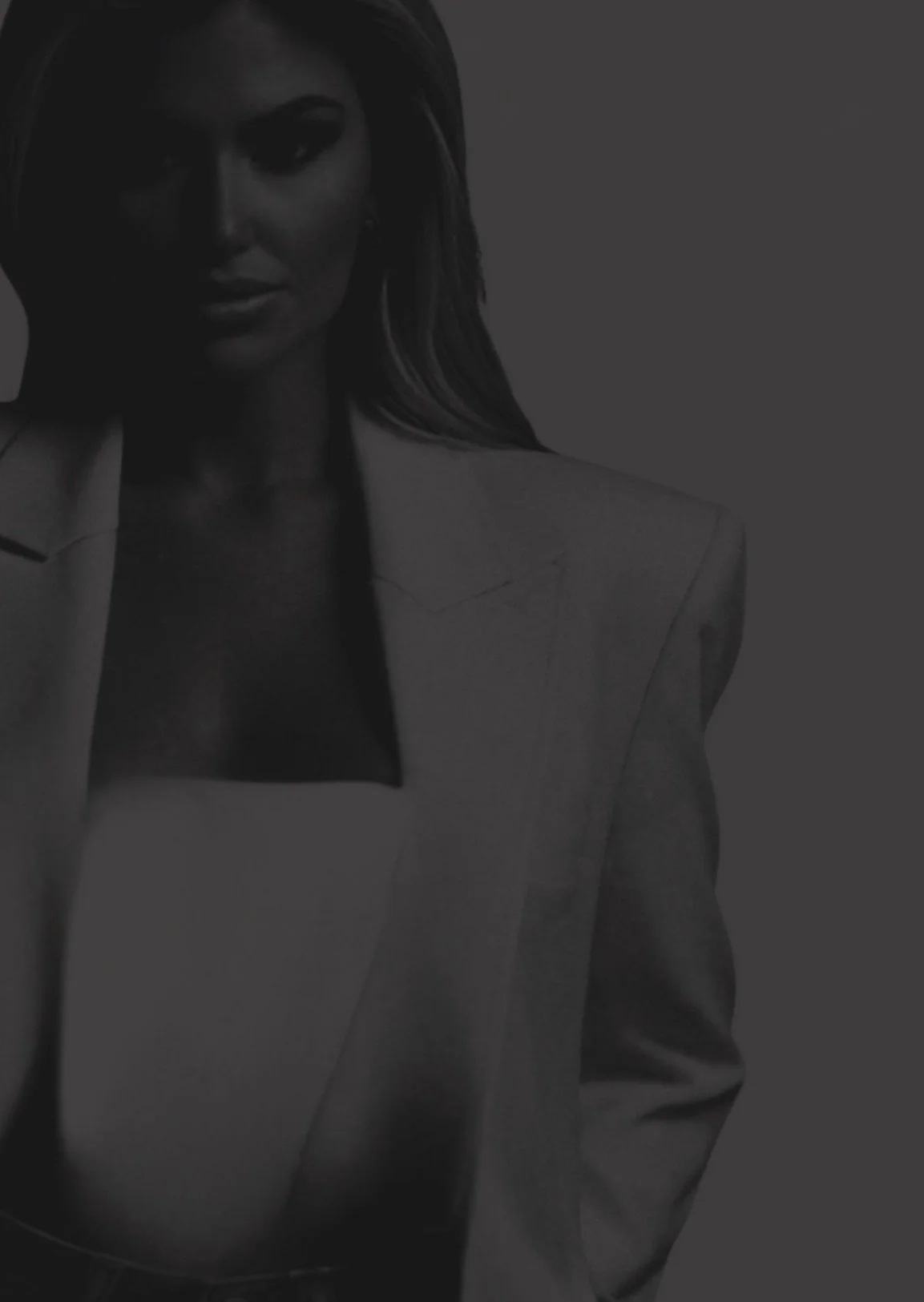 A woman with long hair wearing a blazer and a top, with a confident expression.