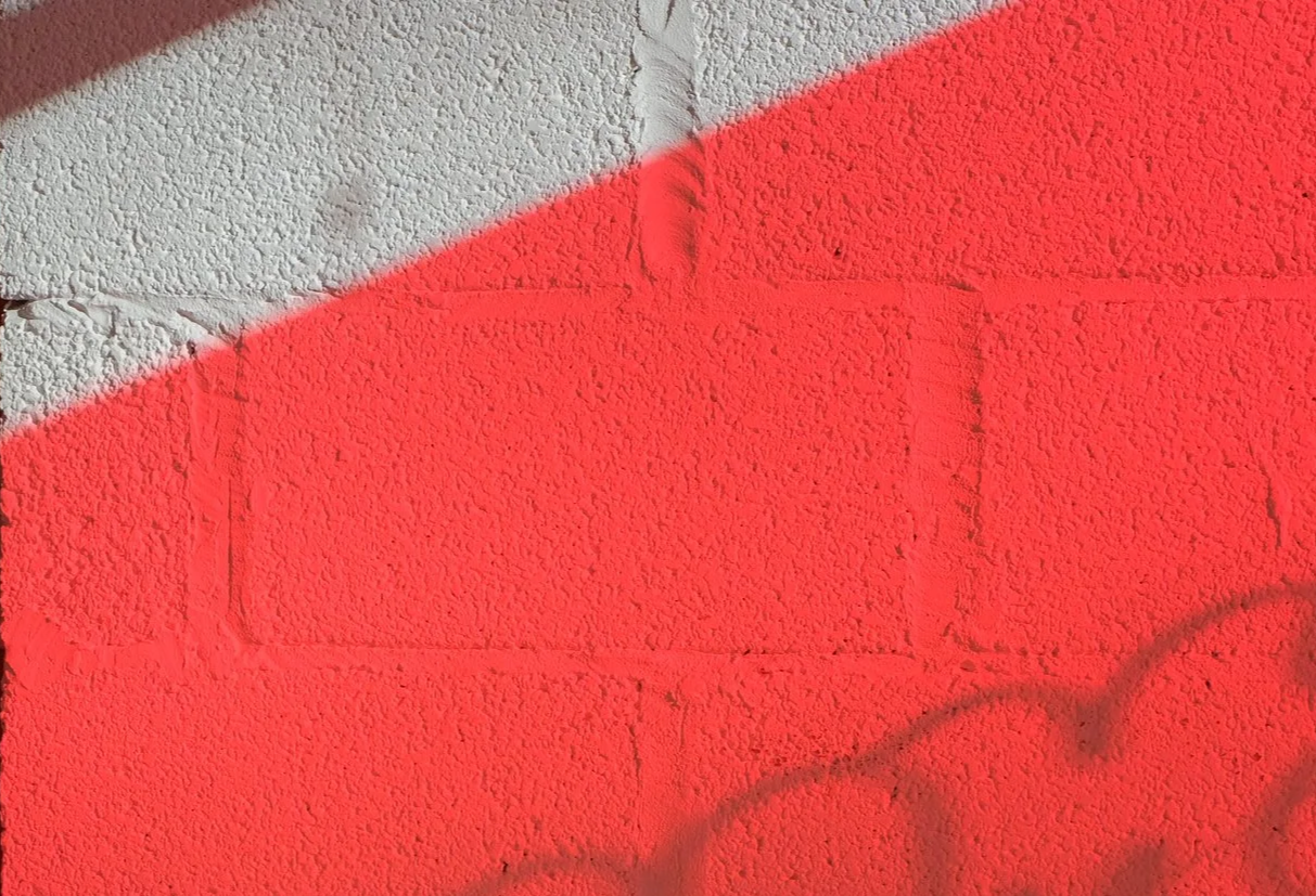 Close-up of a wall with the top half painted white and the bottom half painted red, with a diagonal boundary line between the colors.