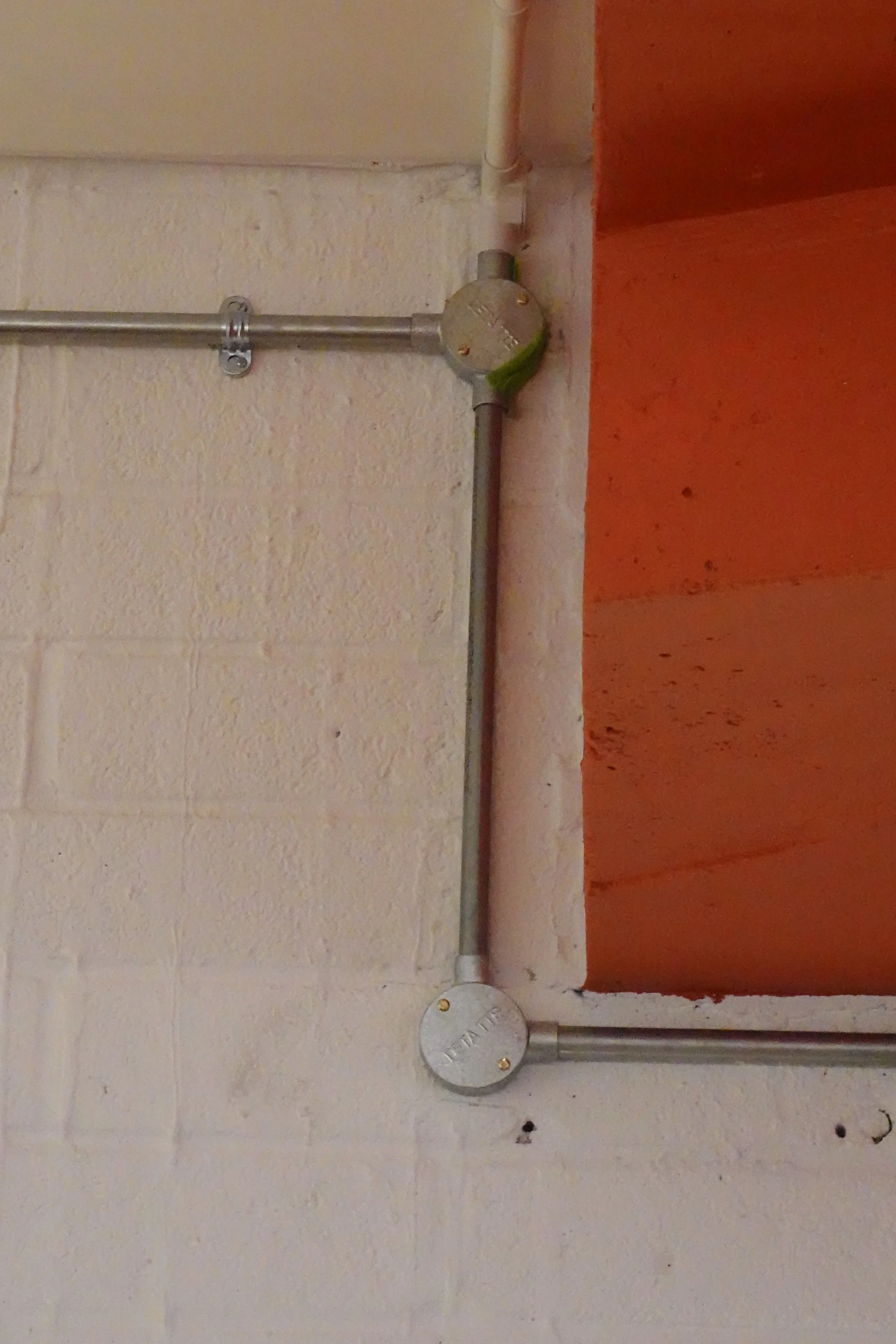 Electrical conduit with junction boxes mounted on a wall near an orange brick opening.