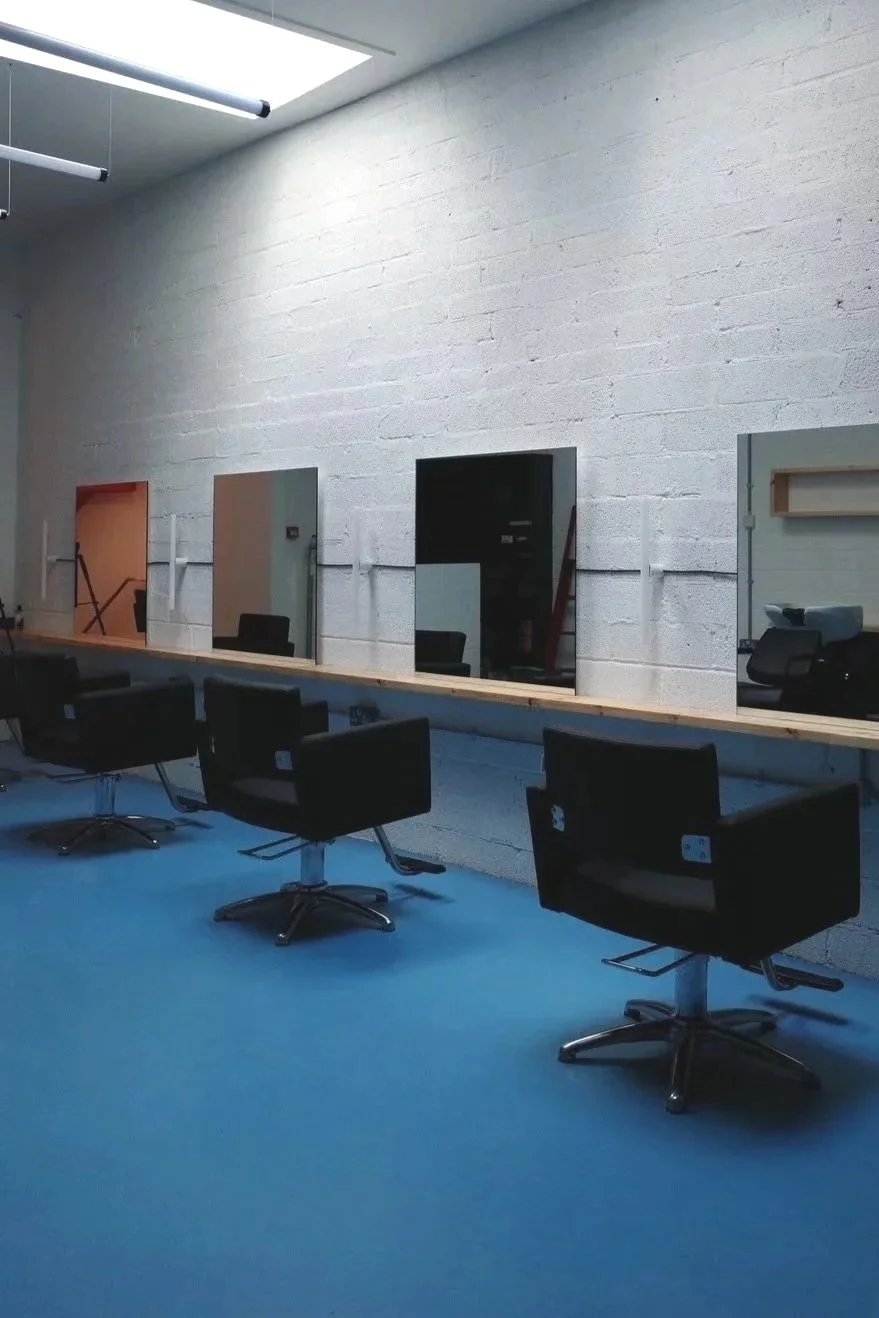 Salon with black chairs, mirrors, white brick wall, and blue carpet.