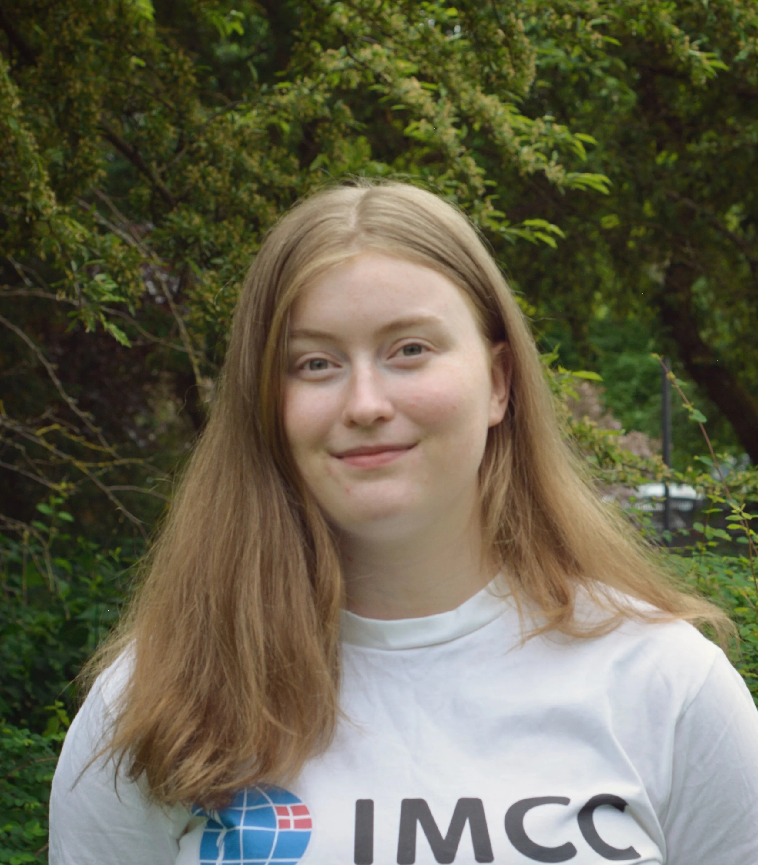 Portræt af Kirstine. Langt brunt hår, smilende, iført hvid IMCC-trøje.
