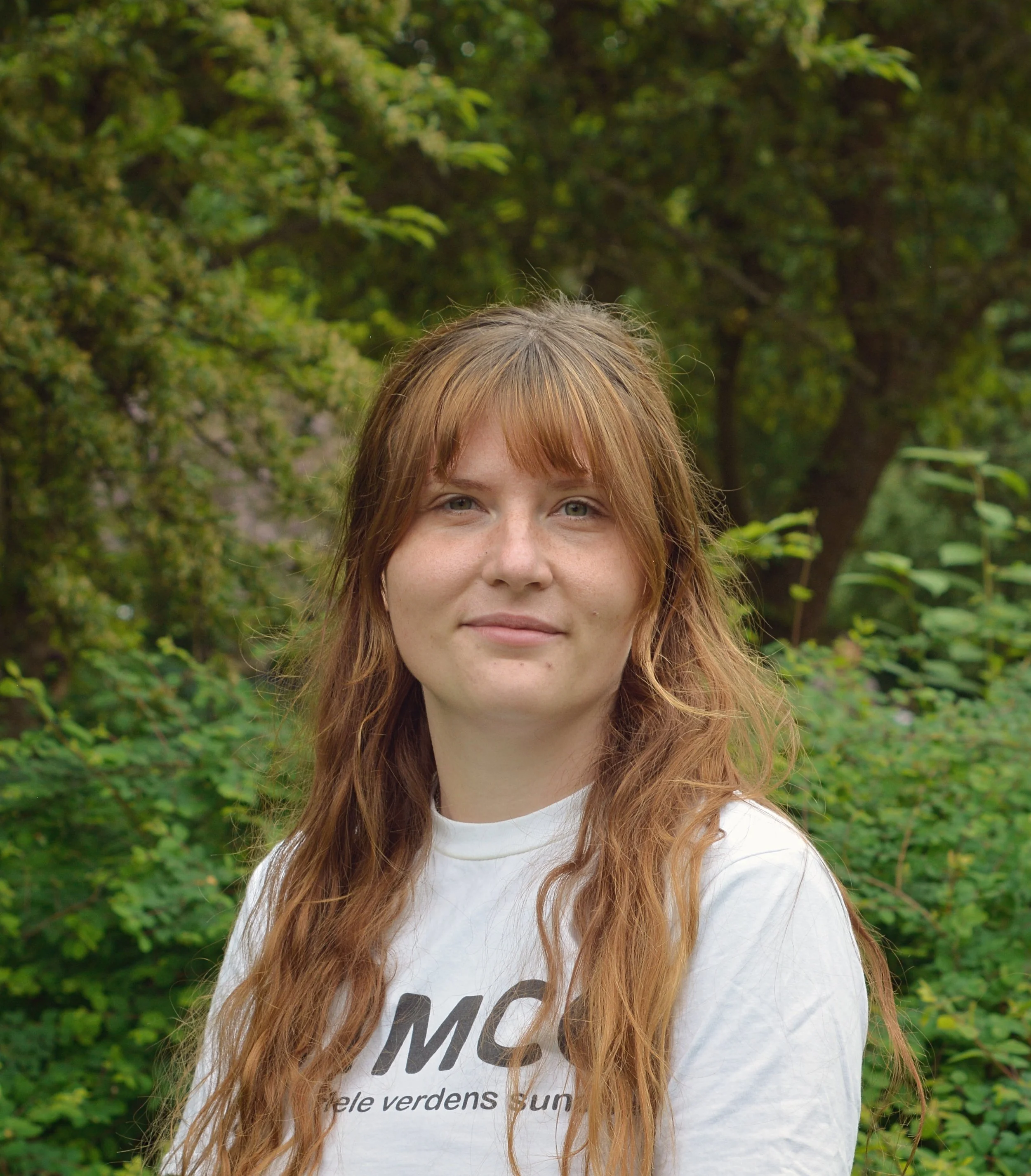 Portræt af  Laura. Langt brunt hår, smilende, iført hvid IMCC-trøje.