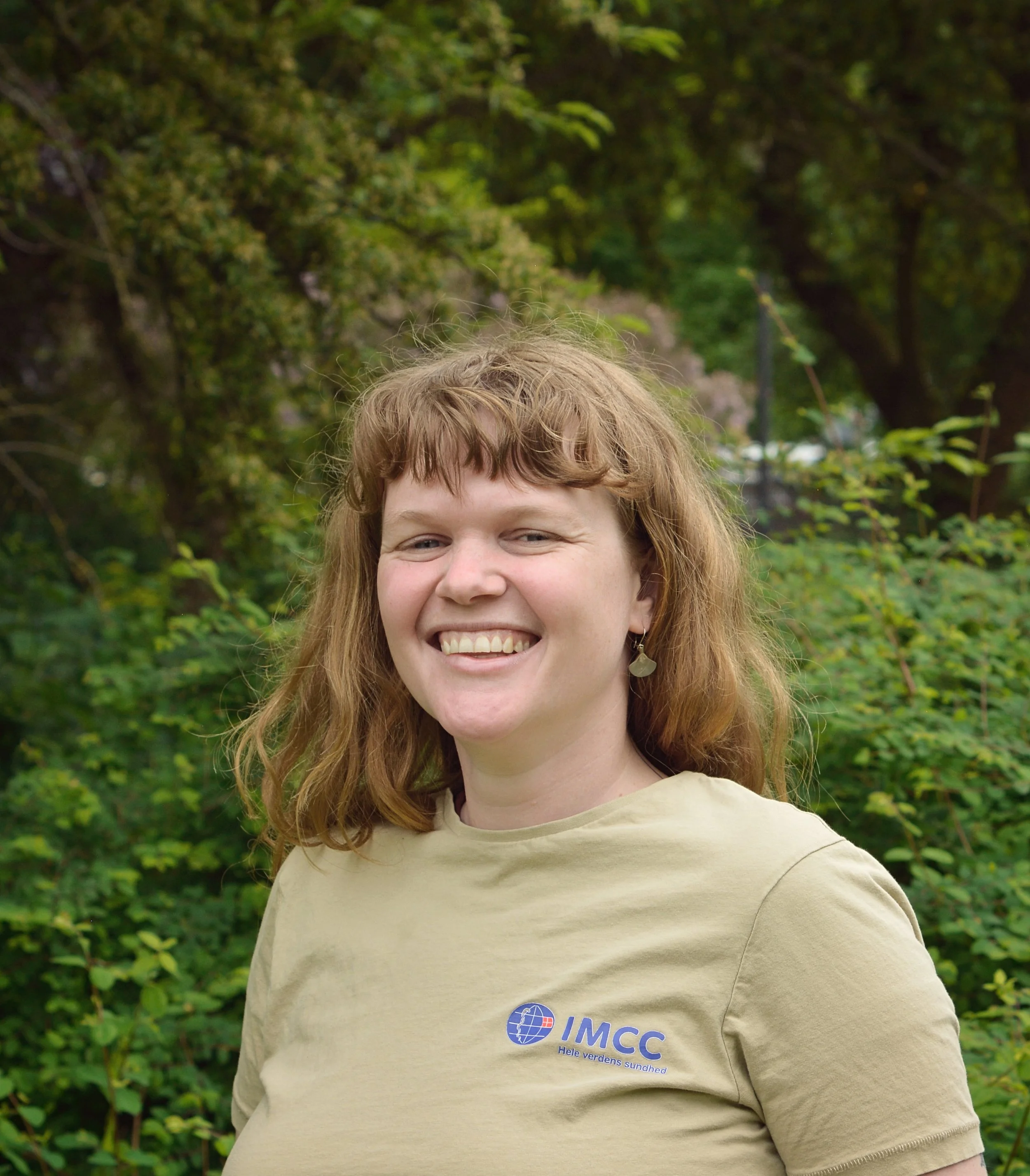 Portræt af Amanda. Skulderlangt krøllet hår, smilende, iført beige IMCC-trøje.