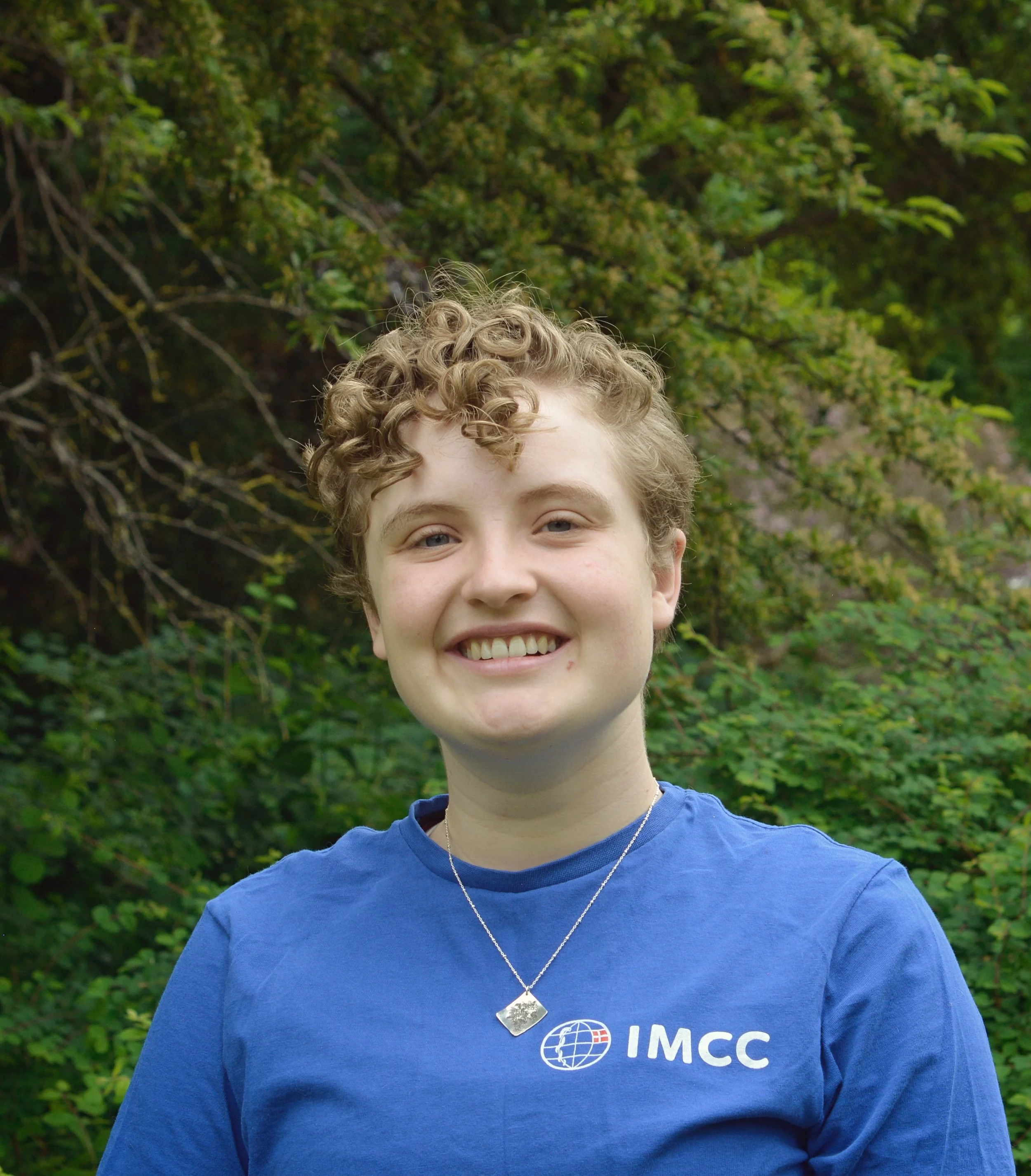 Portræt af Katla. Kort krøllet hår, smilende, iført blå IMCC-trøje.