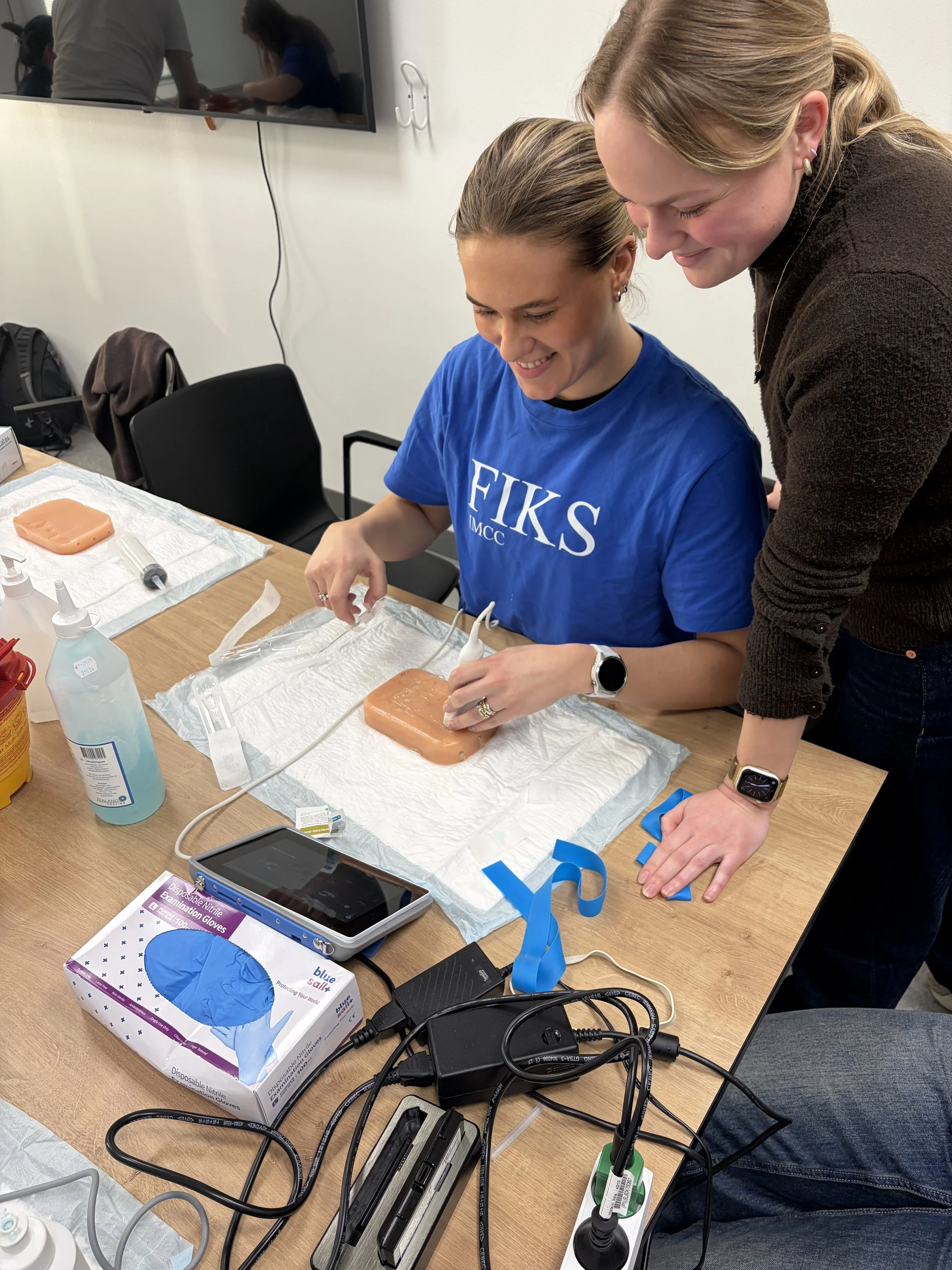 To kvinder ser på en table, som har kirurgiske handsker, markører, og medicinske værktøjer, der bruges til medicinsk procedure.