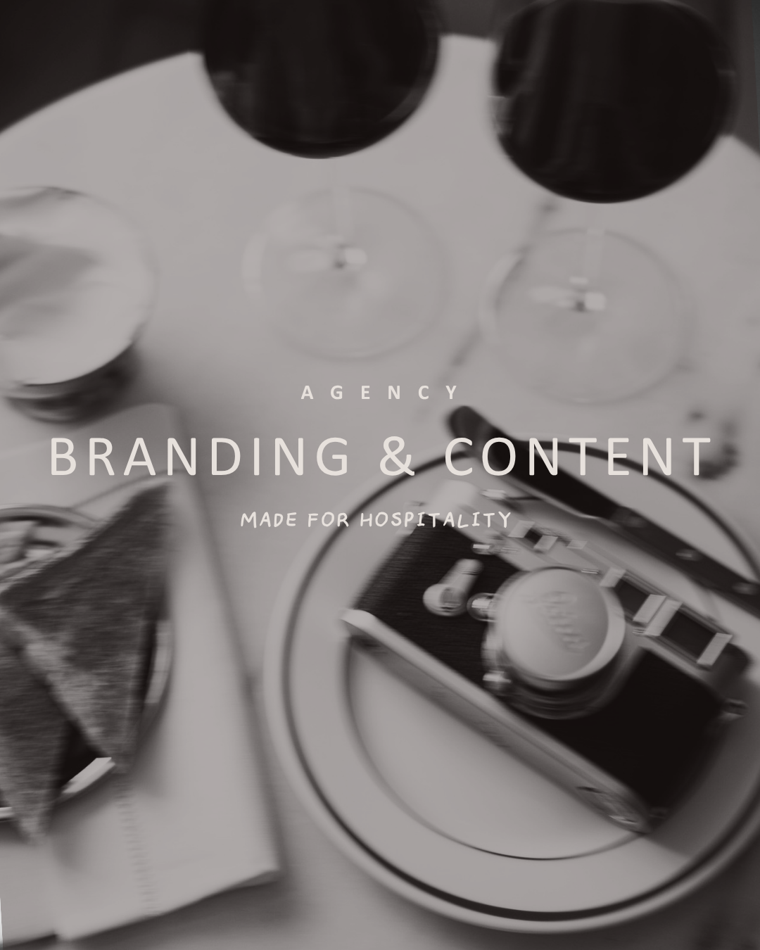LEICA Schwarz-weiß-Bild mit Weinflaschen, Weingläsern, Kamera und Sandwich, Text »Branding & Content für die Hospitality-Branche".