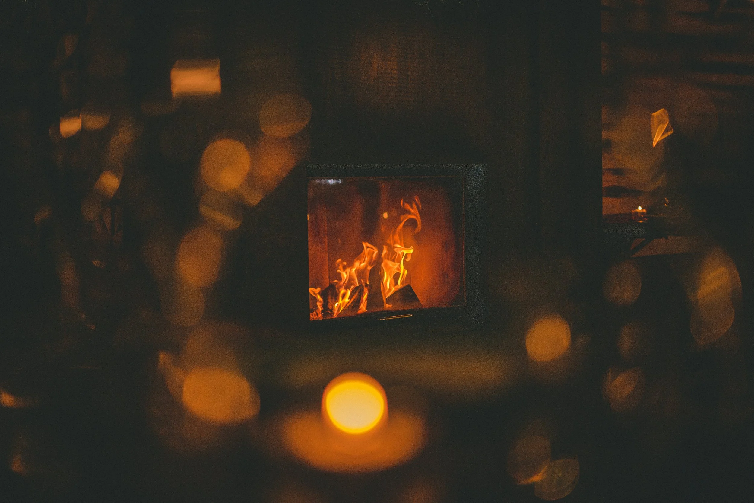 Un feu de cheminée allumé dans une pièce sombre, avec des lumières floues en arrière-plan.