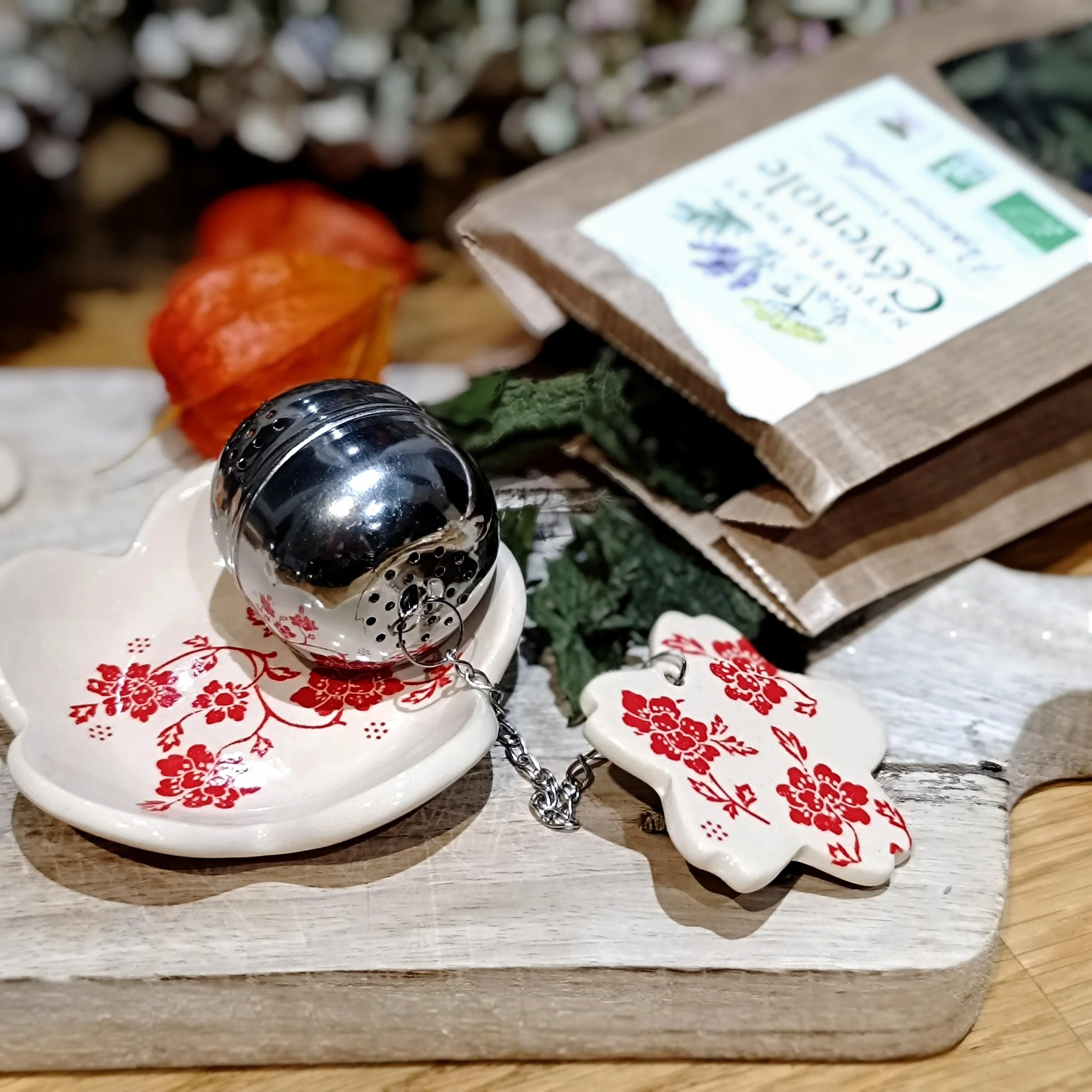Un ensemble de décorations de Noël, comprenant un petit réverbère en forme de boule en métal, des sapins artificiels et des guirlandes vertes sur une table en bois, avec un emballage en carton avec une étiquette blanche et verte.