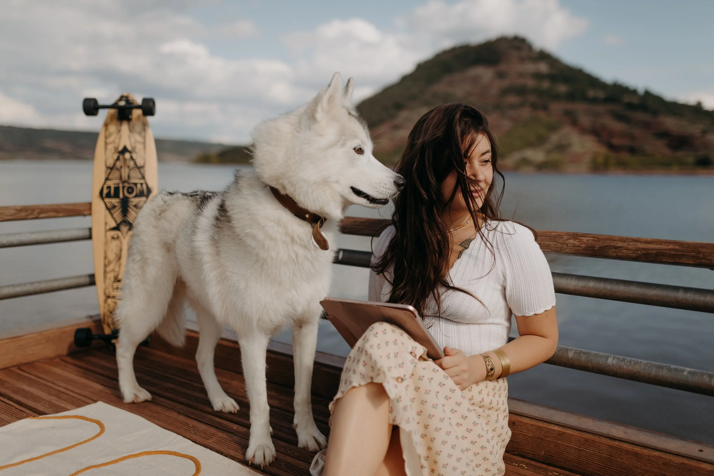 Une femme et un chien husky blanc assis sur une jetée au bord d'un lac avec une montagne en arrière-plan