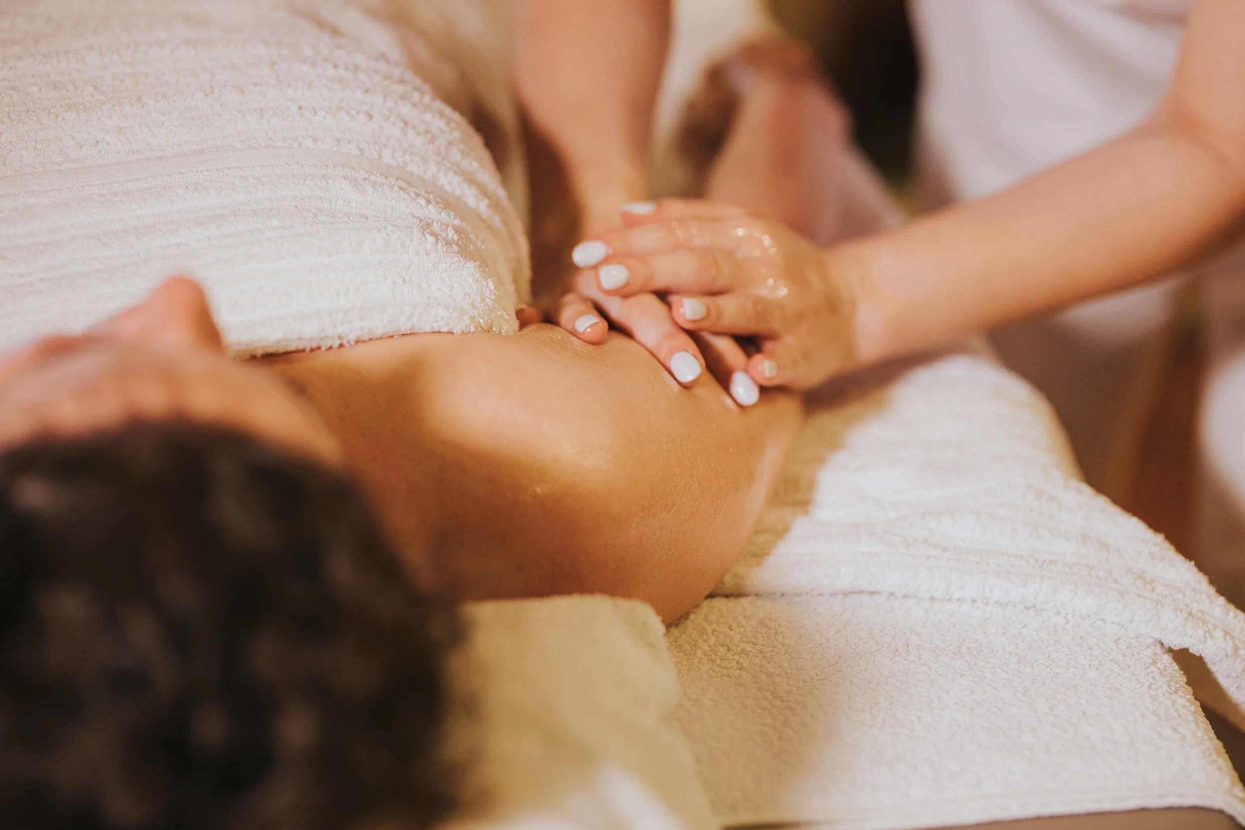 Une personne recevant un massage sur le dos dans un cadre de spa ou de massage, avec des serviettes blanches et une atmosphère relaxante.
