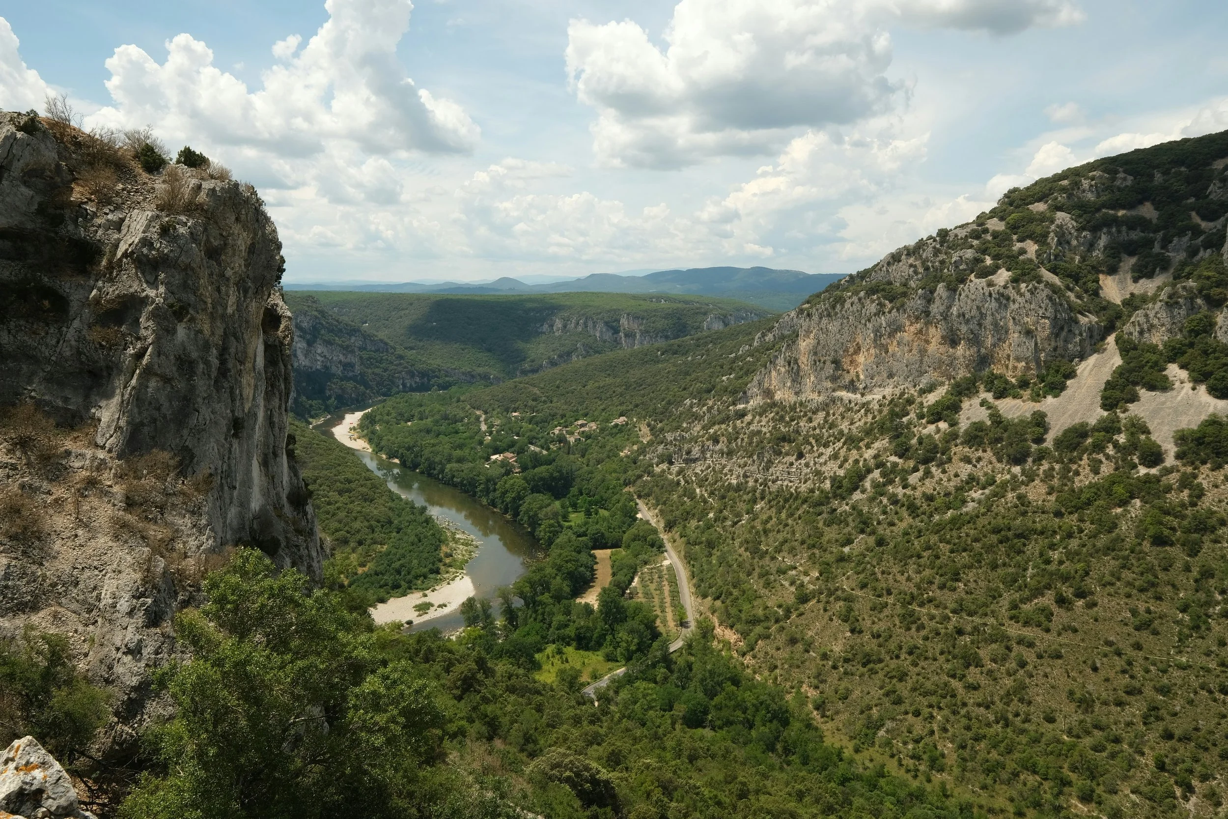 Vallée avec un fleuve serpentant entre des montagnes rocheuses avec des forêts vertes et un ciel partiellement nuageux.