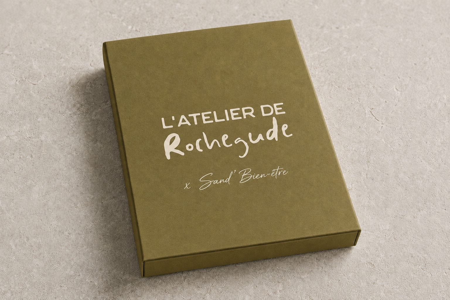 Une boîte verte avec le texte 'L'ATELIER DE Rocheguède x Sand'Bien-être' dessus, posée sur une surface beige.
