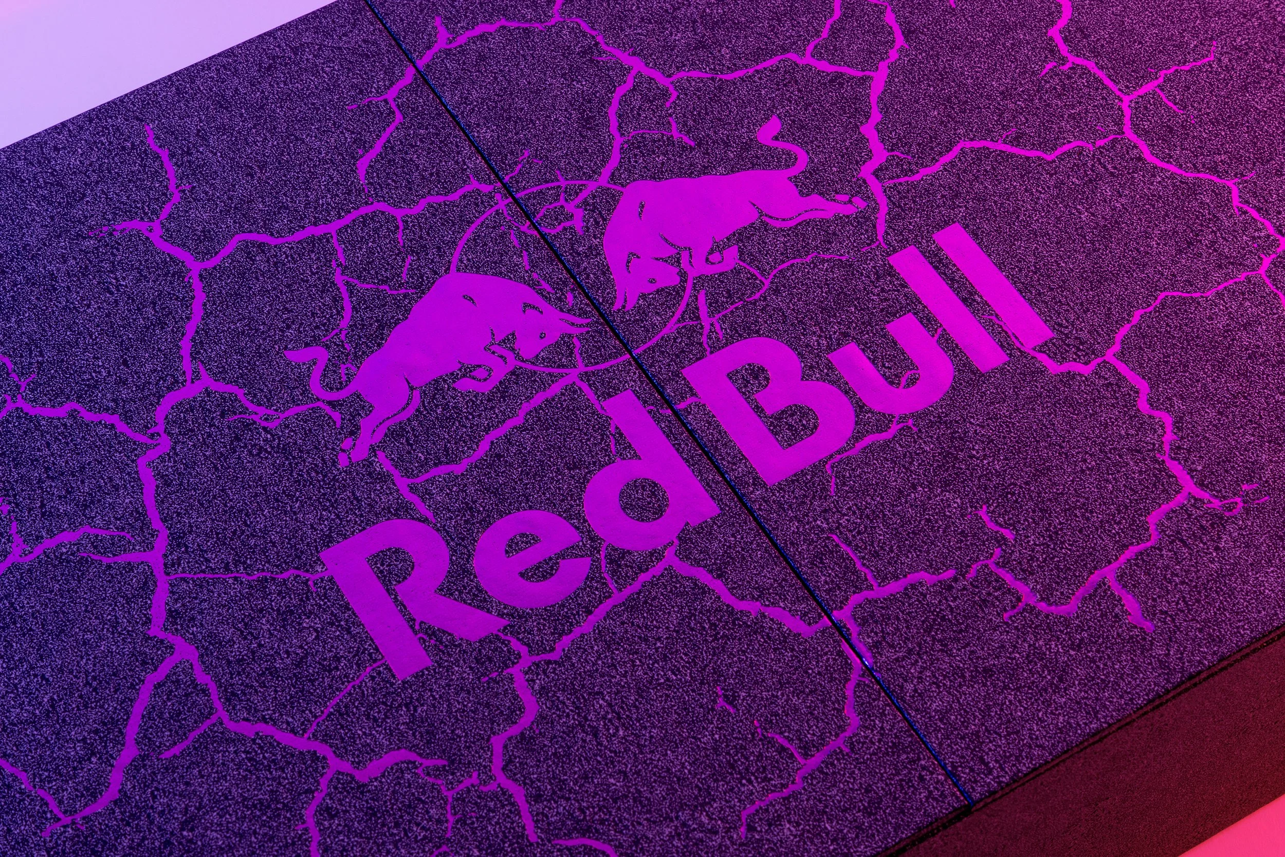 A textured surface with the Red Bull logo and the words 'Red Bull' in bold, purple font. The logo features two Charging Bulls facing each other.