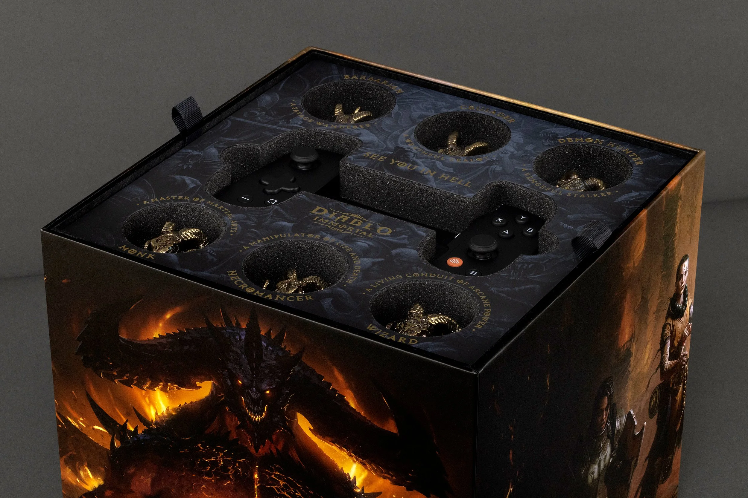 A boxed collector's edition of the game Diablo with themed packaging featuring a flaming dragon on the front, and controllers with gold figurines of demons and monsters inside.