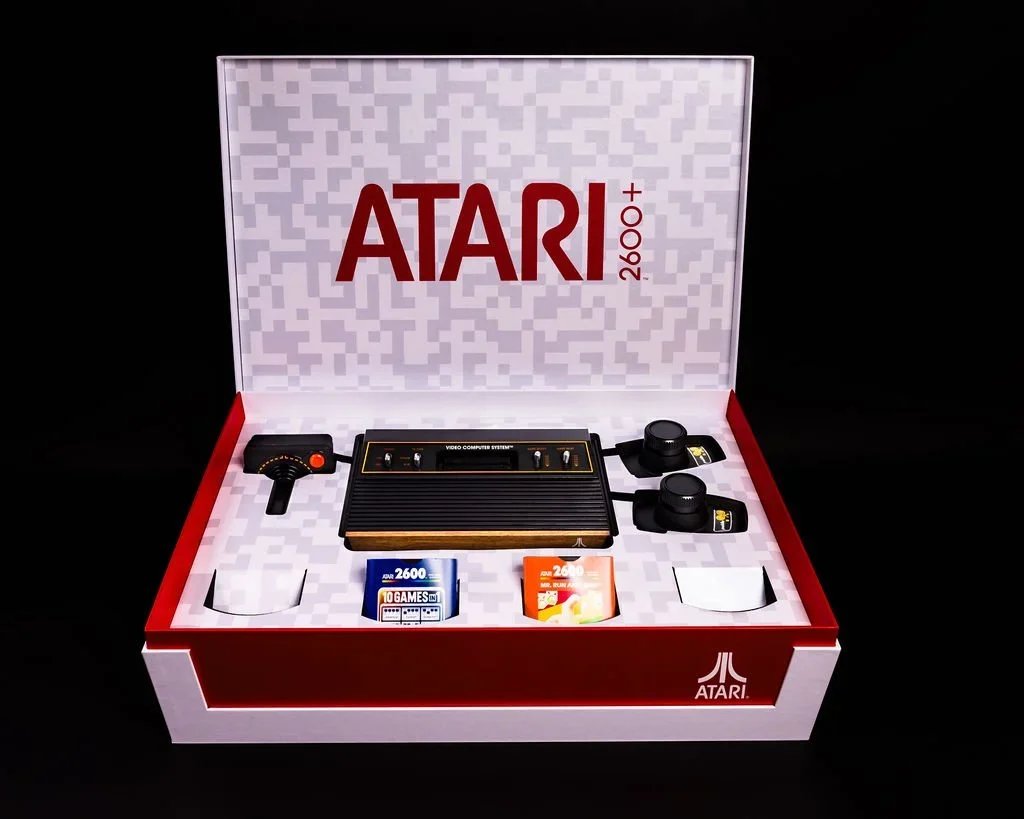ATARI 2600+ gaming console with two controllers, game cartridges, and accessories inside a box with an Atari logo and branding.