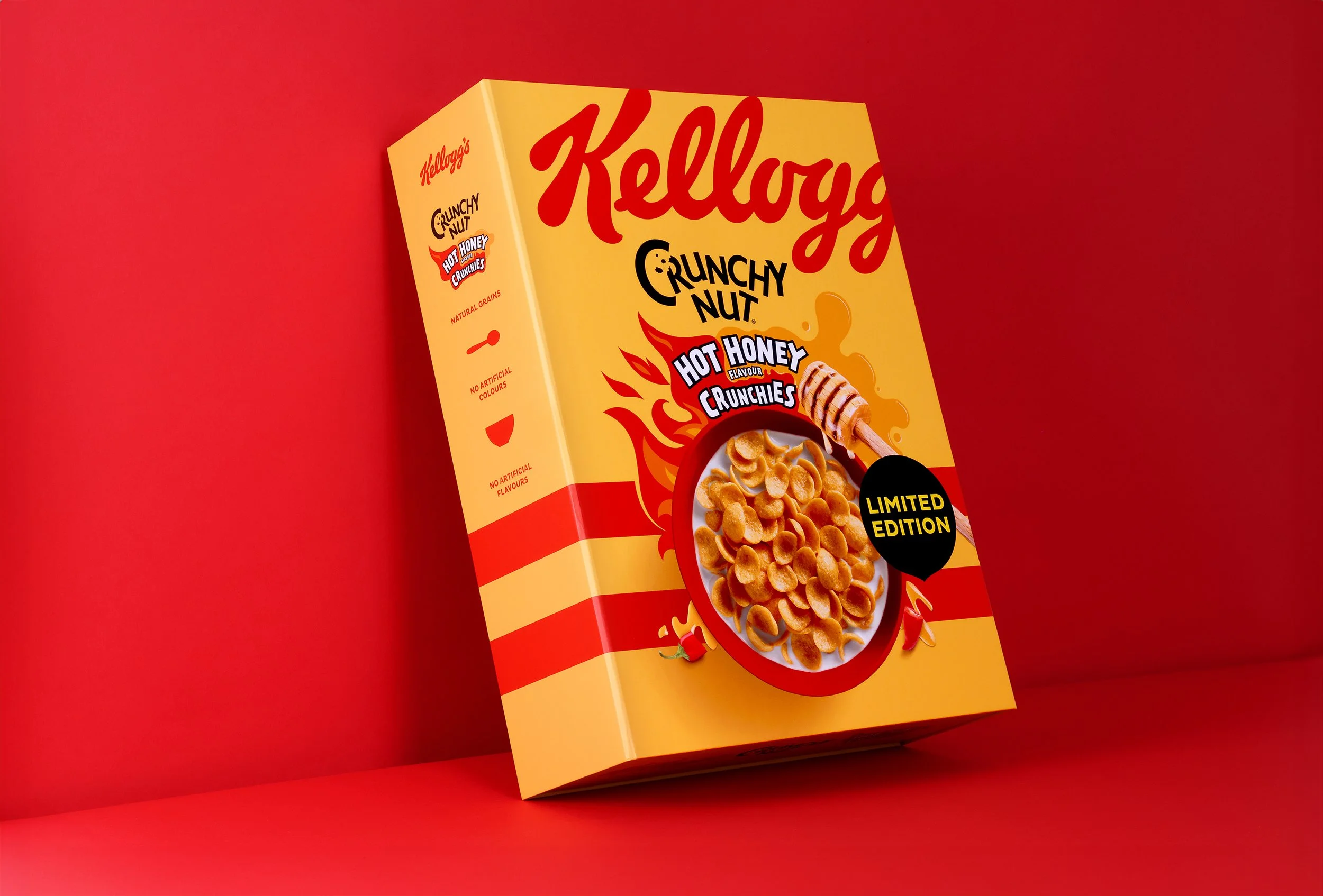 A box of Kellogg's Crunchy Nut Hot Honey flavor cereal with a yellow and red design, featuring an image of cereal in a bowl with milk and a honey dipper, and a black label indicating it is a limited edition.