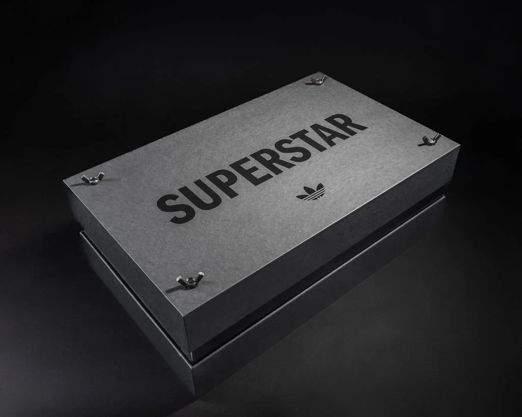 Gray metal box with the words 'SUPERSTAR' and a small Adidas logo printed on the top, secured with four bolts.